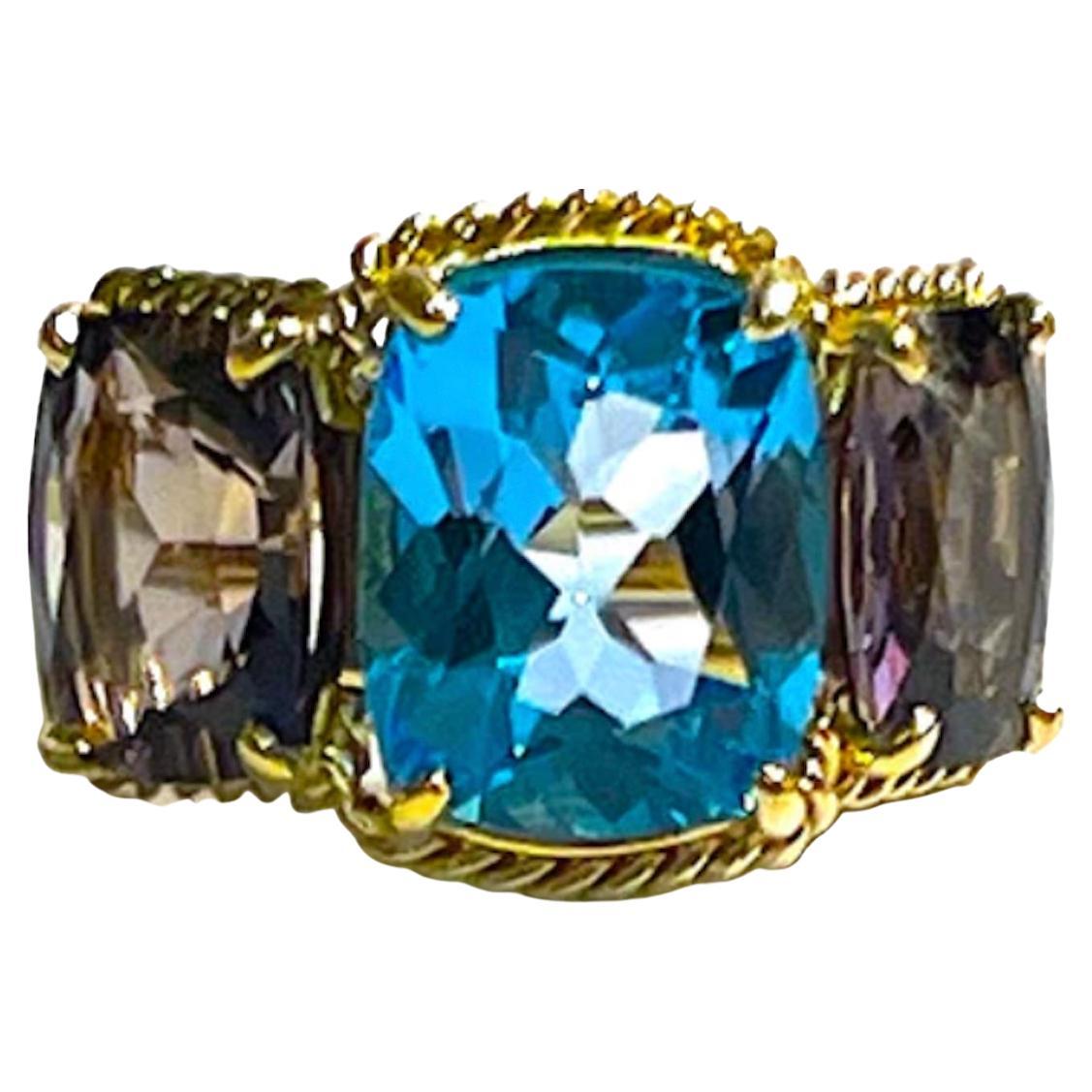 Elegant 18kt White Gold Three Stone Ring with Rope Twist Border with split shank detail. The ring features a center faceted cushion cut Blue Topaz and two cushion cut Iolite stones surrounded by twisted gold rope. The center stone measures 5/8
