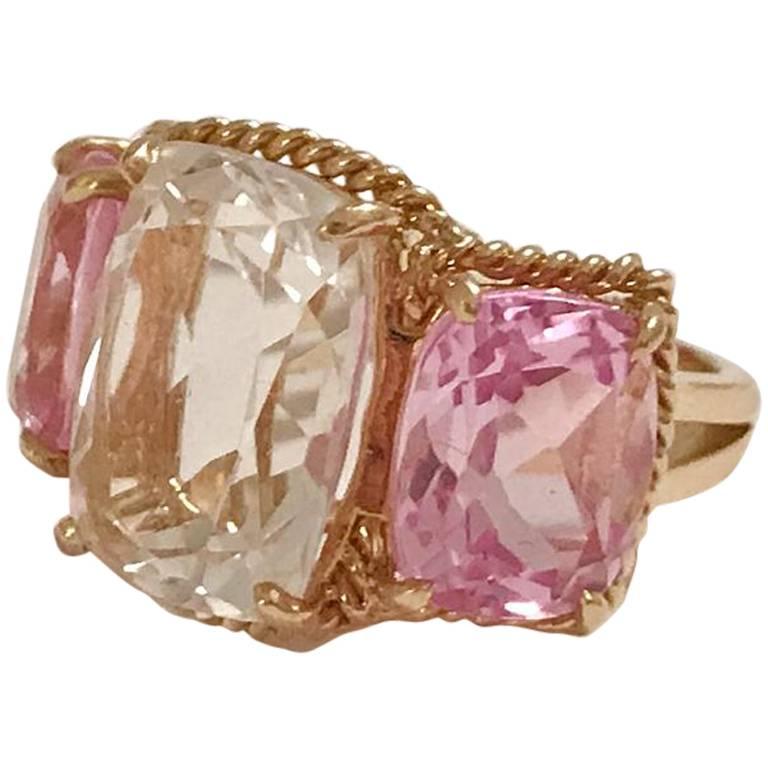 Elegant 18kt Yellow Three Stone Ring with Rope Twist Border with split shank detail. The ring features a center faceted cushion cut Pale Pink Topaz and two cushion cut bright Pink Topaz surrounded by twisted gold rope. The center stone measures 5/8