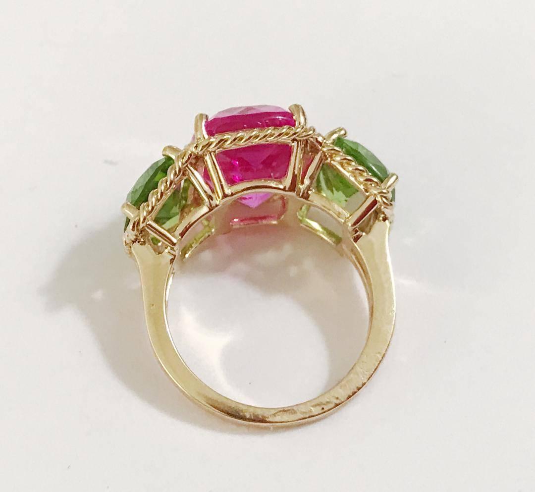 Elegant 18kt Yellow Three Stone Ring with Rope Twist Border with split shank detail.

The ring features faceted cushion cut Hot Pink Topaz and Peridot stones surrounded by twisted gold rope. The center Pink Topaz measures 5/8