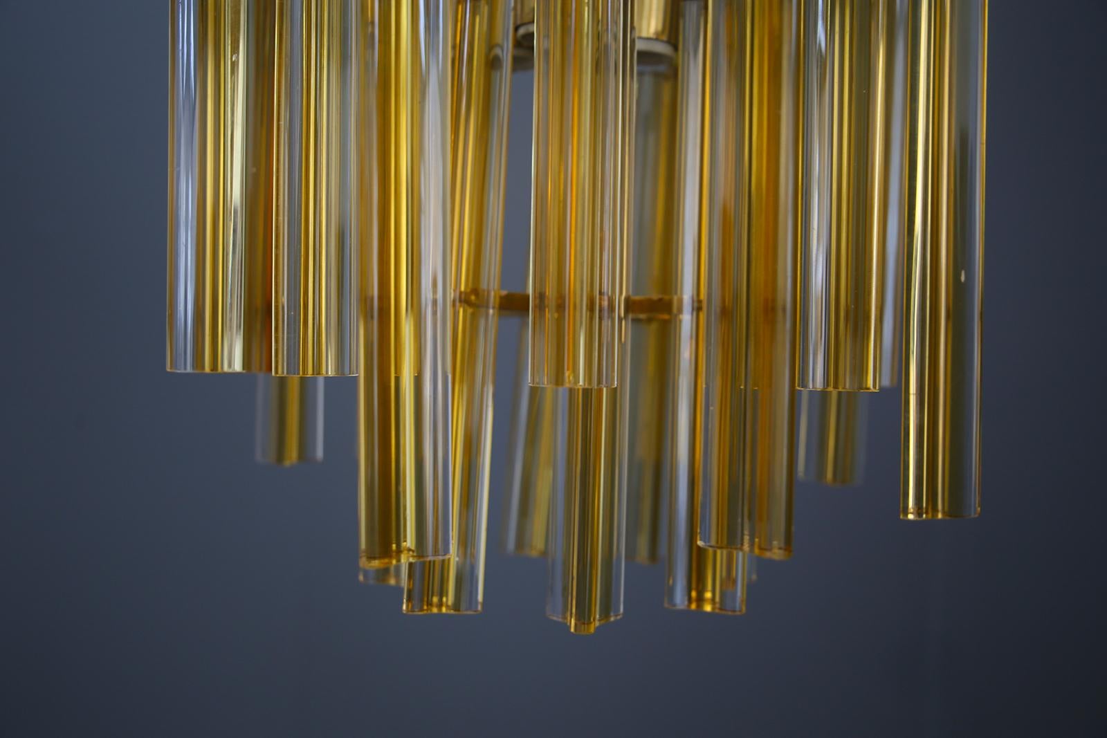 Elegant chandelier from the Venini factory in glass and brass from the 1950s. The chandelier is in perfect original condition. The pendant is composed of 24 parallelepipeds with a triangular base in solid gilded glass. The glasses are hand ground in
