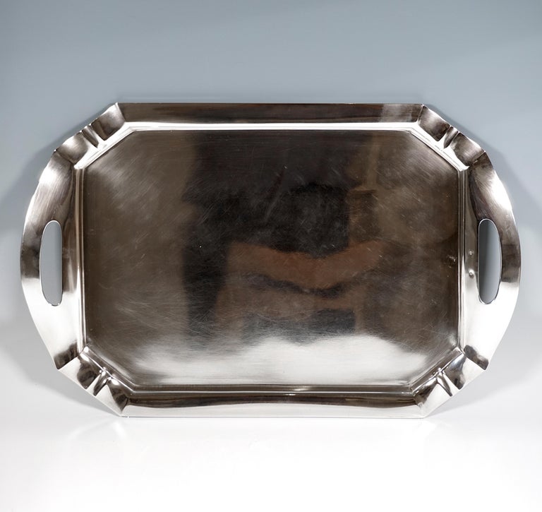 Rectangular shaped silver tray in a smooth, simple design with a raised, flared edge and beveled corners with a raised groove in the middle, rounded, slightly curved extension of the edge piece on the broad sides with incised