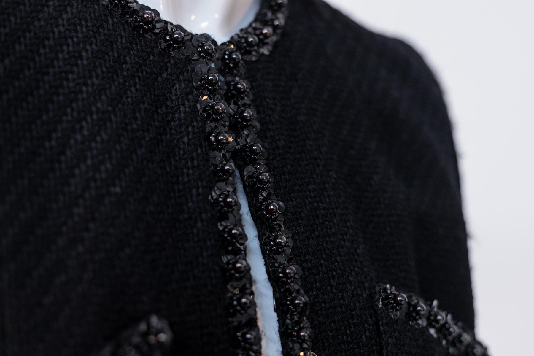 Sehr elegantes schwarzes Vintage-Stoffkleid aus den 1990er Jahren, hergestellt in Italien. Das Muster erinnert sehr an den Chanel-Schnitt. Das Kleid besteht aus zwei Teilen: Jacke und Rock.
Die Jacke hat lange Ärmel und einen hohen U-förmigen,