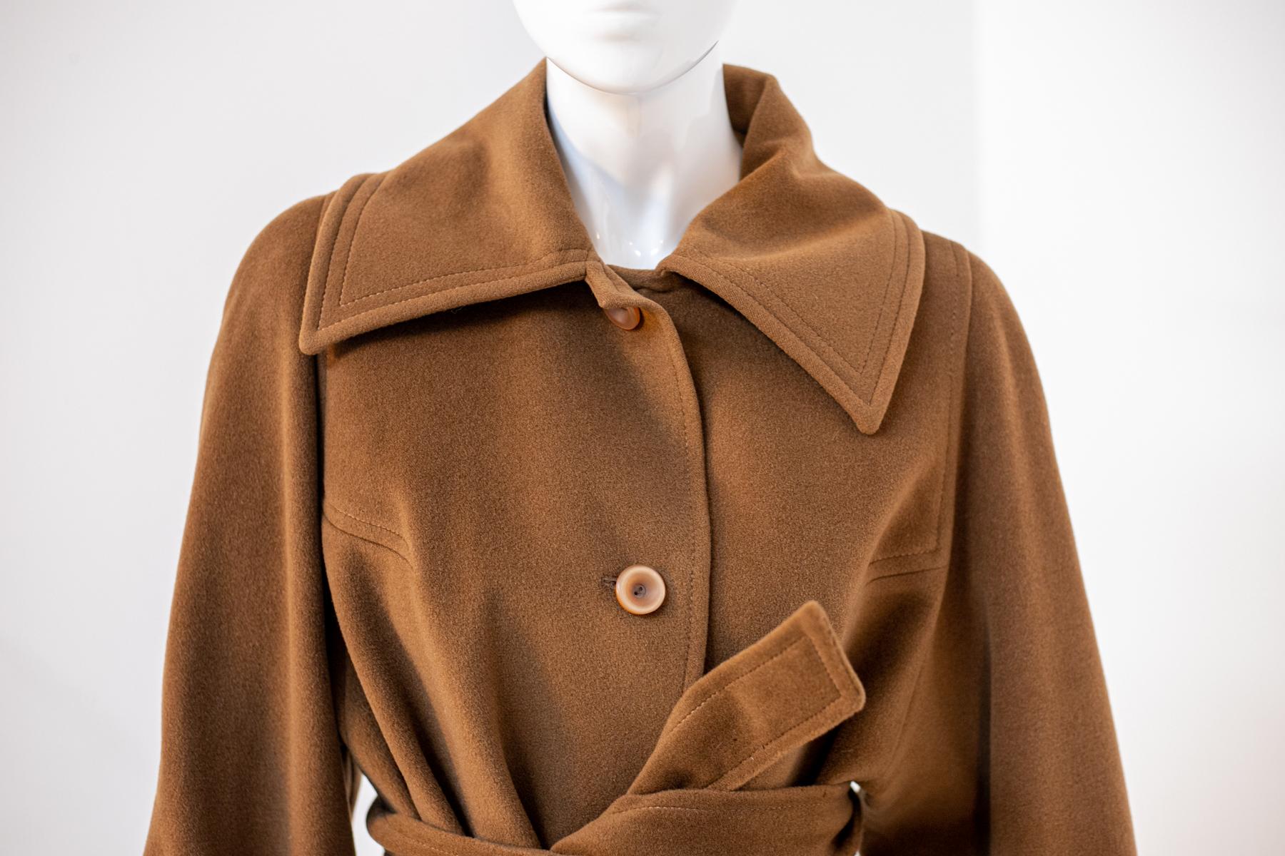 Eleganter Wollmantel, entworfen in den 1980er Jahren, hergestellt in Italien.
Der Mantel ist ganz aus warmer hellbrauner Wolle, Farbe camel. Es reicht bis zu den Knien und hat lange Ärmel. Die Ärmel sind groß genug, um dicke Pullover zu tragen, aber