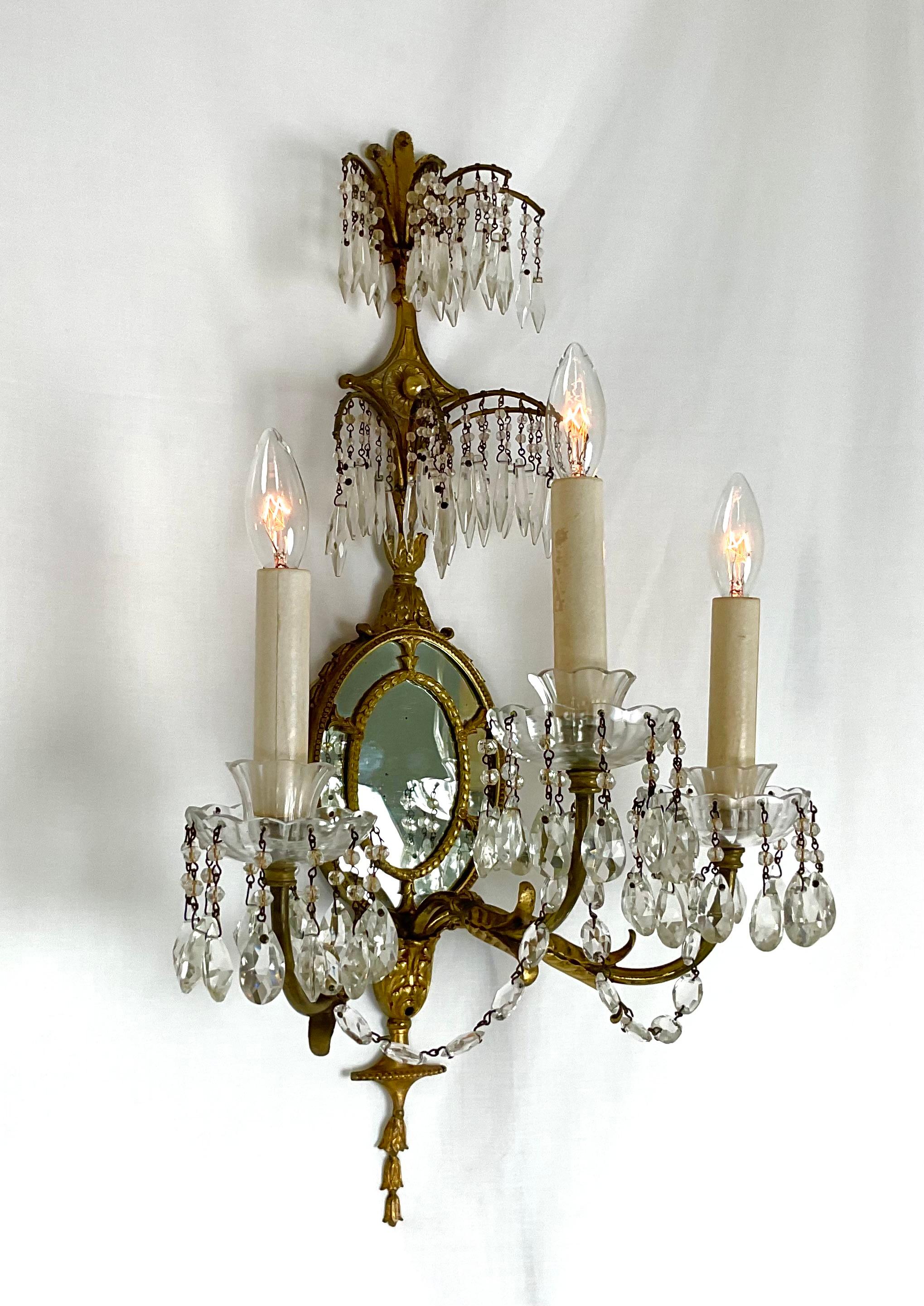 Add timeless charm and sophistication to your space with this exquisite vintage French-style wall sconce. Featuring ornate brass detailing, two graceful candle-style arms, and delicate crystal prisms that catch the light beautifully, this piece