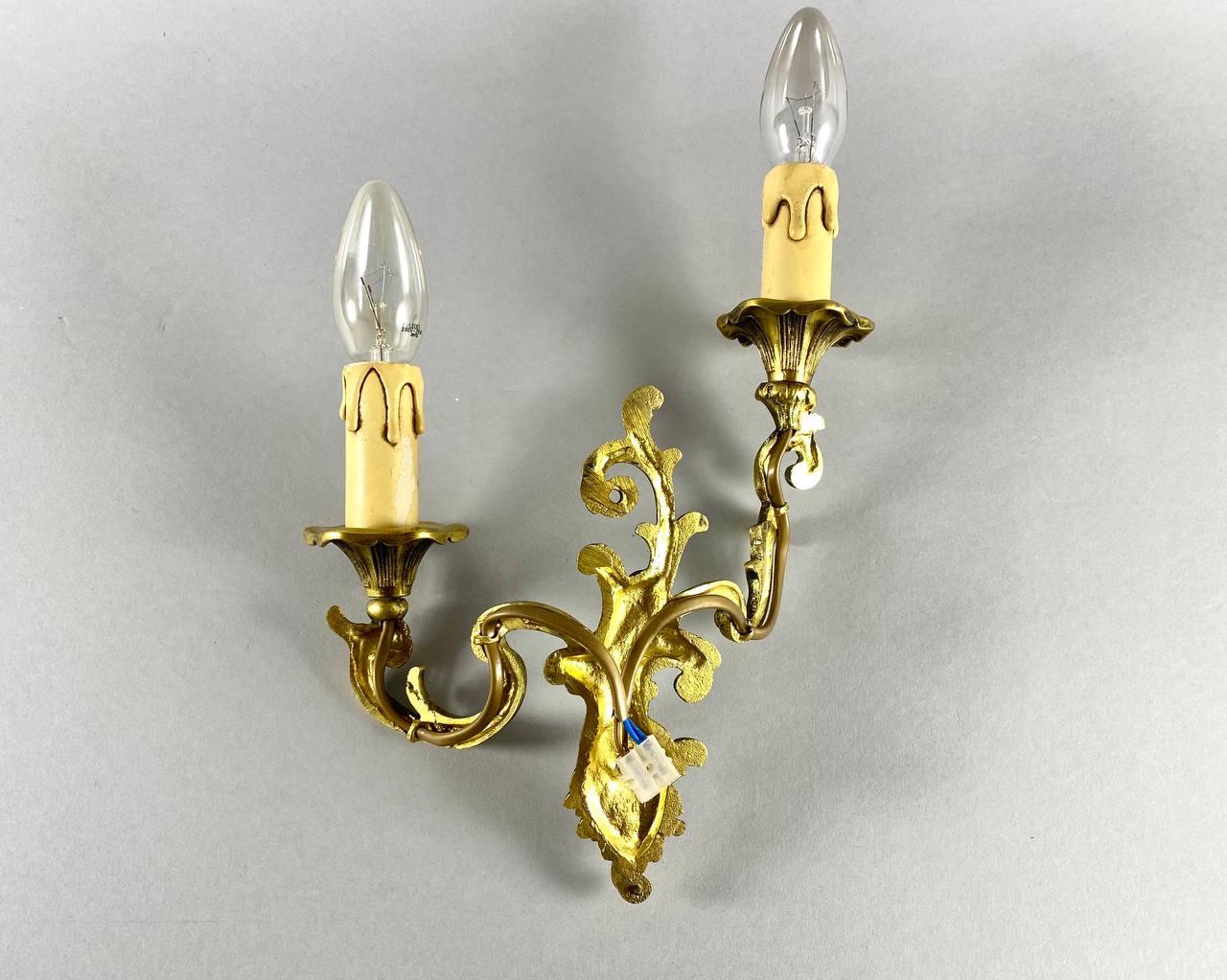 Elegant vintage wall sconce. Made of gilt brass, artistic casting.
Floral motif with classic swirl.

The wall sconce consists of a base and two curved arms emanating from it, skillfully finished with chasing by hand.

The horns of the sconce