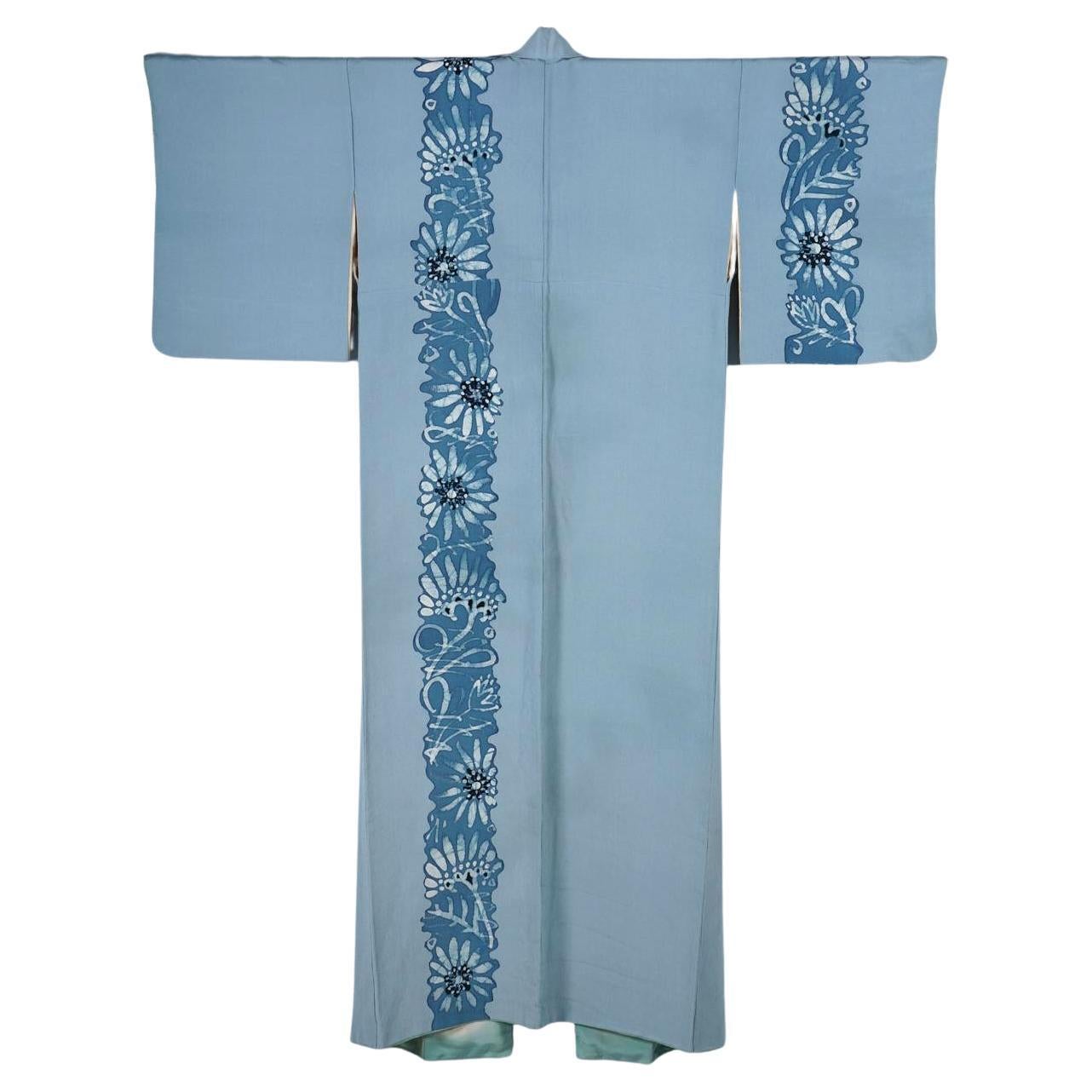 Ein japanischer Seidenkimono in Hellblau mit auffälligem Blumenmuster. Das Kleidungsstück ist aus kreppartiger Seide handgenäht und wird auf ca. 1940-60 datiert. Das Kleidungsstück ist spärlich, aber wirkungsvoll mit Bändern aus Gänseblümchenketten