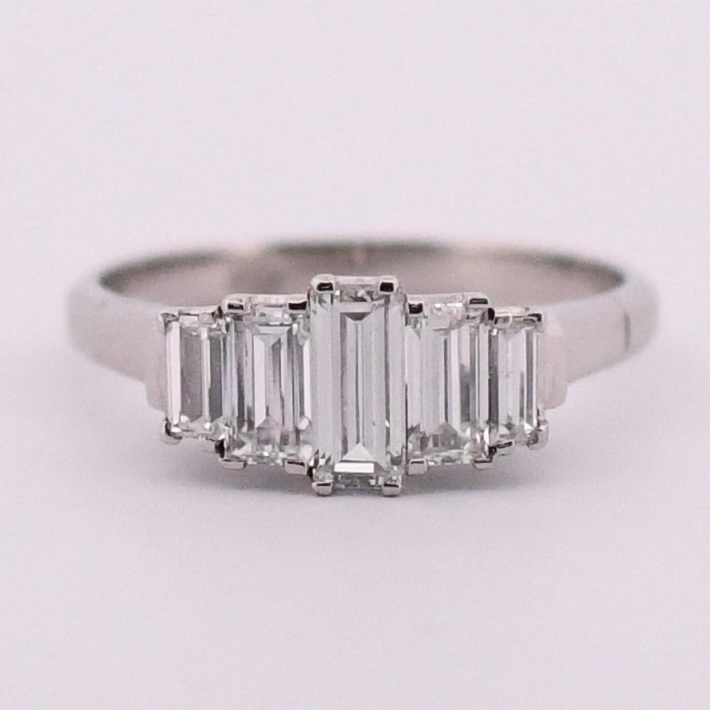 Exuding timeless charm, this platinum vintage ring showcases refined simplicity and exceptional craftsmanship. Its tapered shanks lead to a classic gallery adorned with five exquisite F-colored baguette diamonds. Ideal as an engagement ring matched