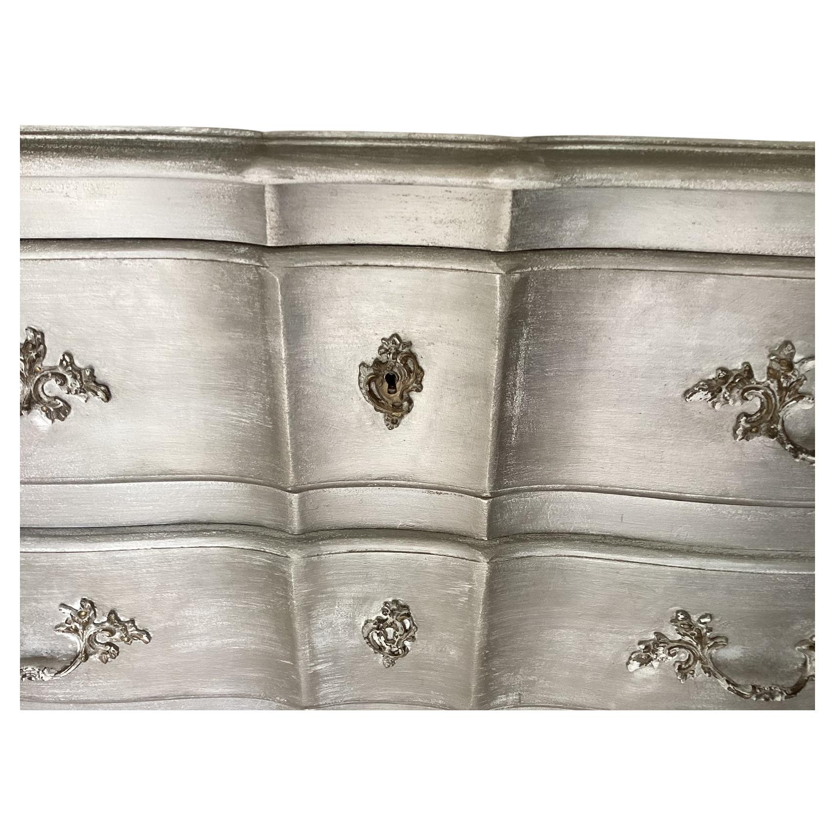 Traditional French chest given a new glam look with shimmering silver paint. There are 3 drawers for storage, original drawer pulls and key entry hardware. The front is slightly wavy for added elegance and the sides feature arched panels.

Danielle