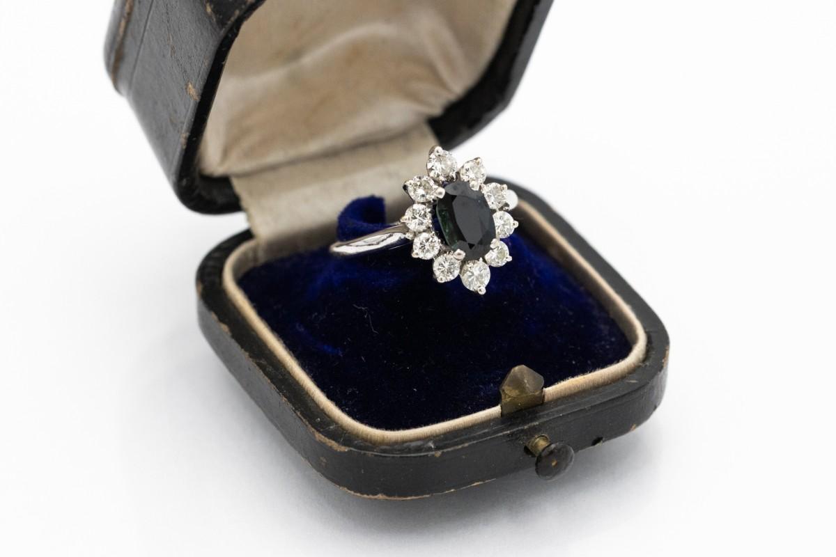 Luxurious ring made of 18-carat white gold (0,750). Its central point is an oval sapphire with an intense dark blue color and an impressive weight of 1.50 ct. The sapphire is surrounded by 10 brilliant-cut diamonds weighing 0.90ct (F-G color and