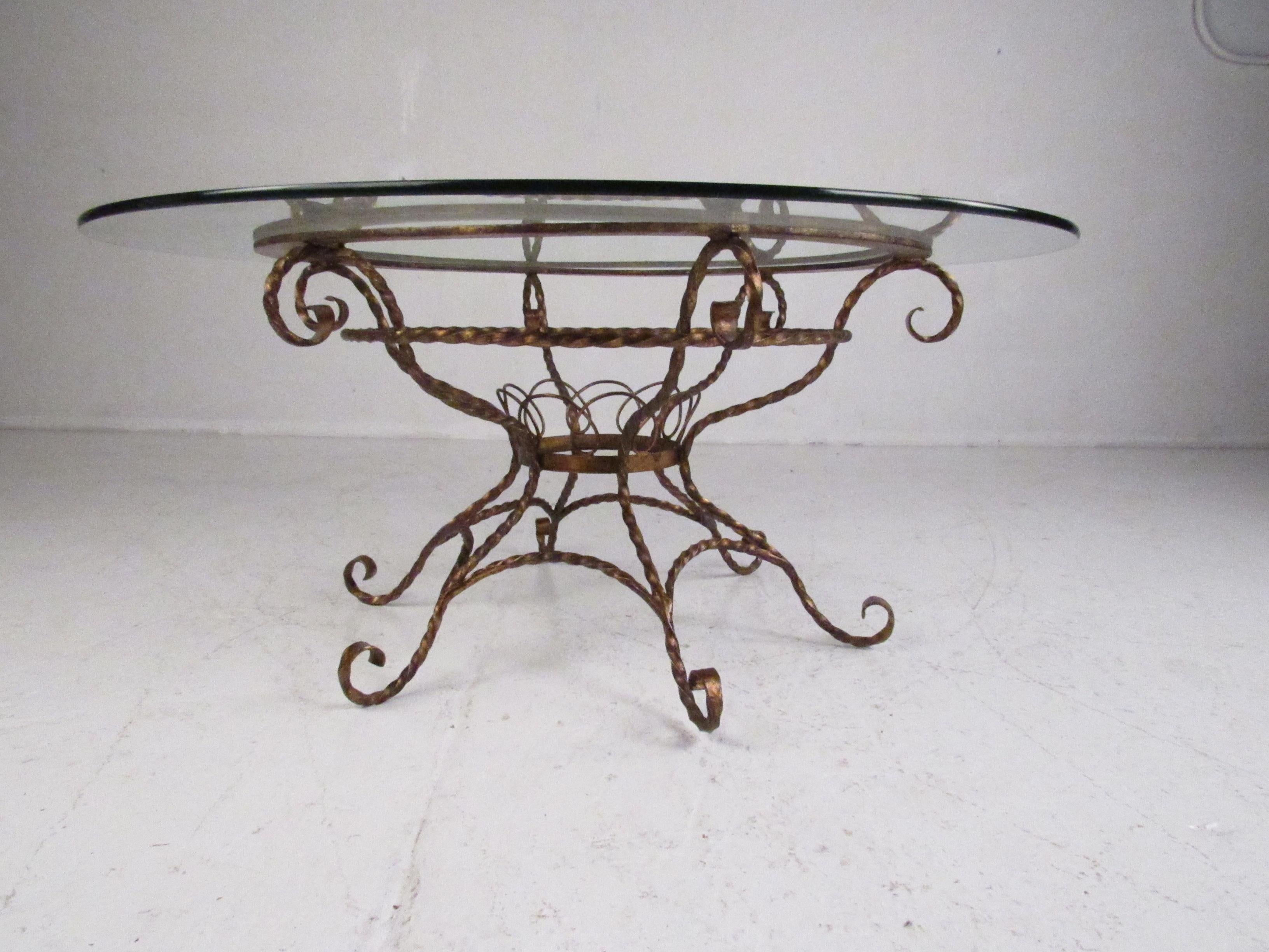 This stunning Mid-Century Modern coffee table features exquisite scroll detail and a lovely brass colored finish. A sleek design with a large circular glass top and splayed legs. A very unique and elaborate piece that is sure to make a lasting