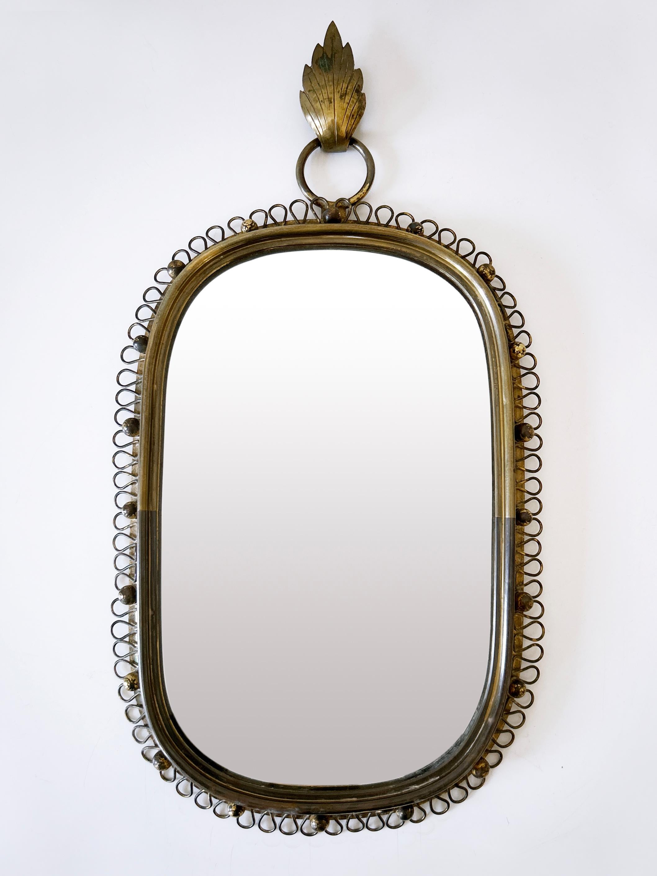 Gorgeous, highly decorative Mid Century Modern wall-mounted mirror with loop brass frame. Designed by Josef Frank for Svenskt Tenn, Sweden, 1950s.

Executed in brass, mirror glass and metal.

Dimensions:
Height: 17.72 in (45 cm)
Width: 9.45 in (24