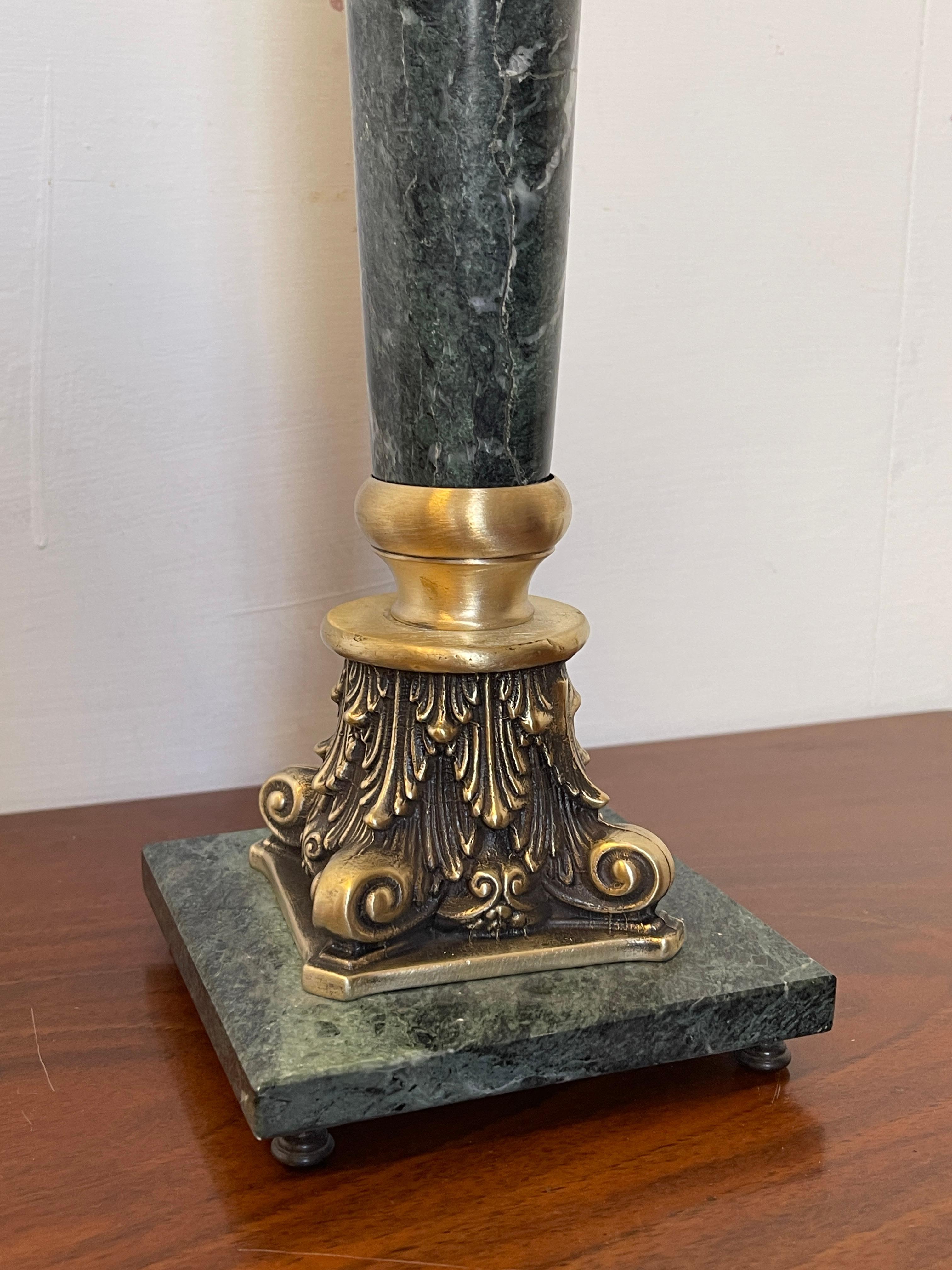 Ein eleganter und raffinierter Kerzenständer, der die Solidität des grünen Marmors mit der Schönheit der vergoldeten Bronze verbindet. Die schlanke Säule steht auf einem massiven Sockel mit reichhaltigen Details aus Bronze, während der obere Teil