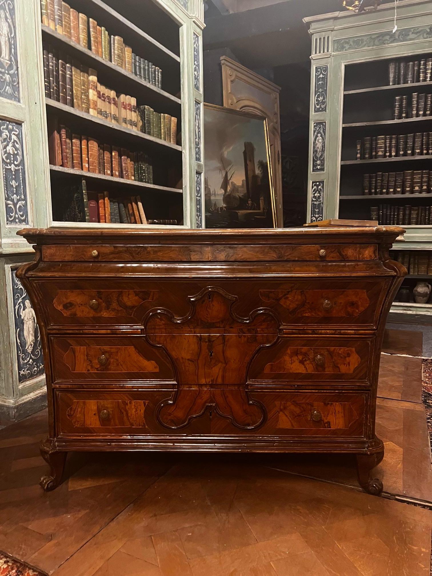 Elegante comò antico in legno massello di noce e radica di noce, Caratterizzato da una ricca lavorazione intarsiata. La fachada presenta una refinada decoración central incrustada, típica de la mejor tradición artesanal de la época.
Las venas