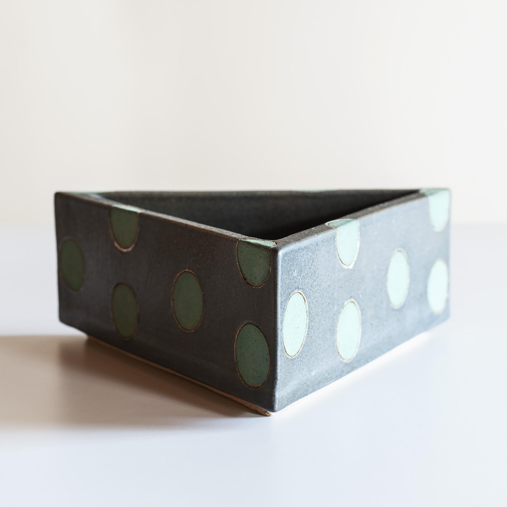 Stoneware vessel with green polka dots on earthen grey background.