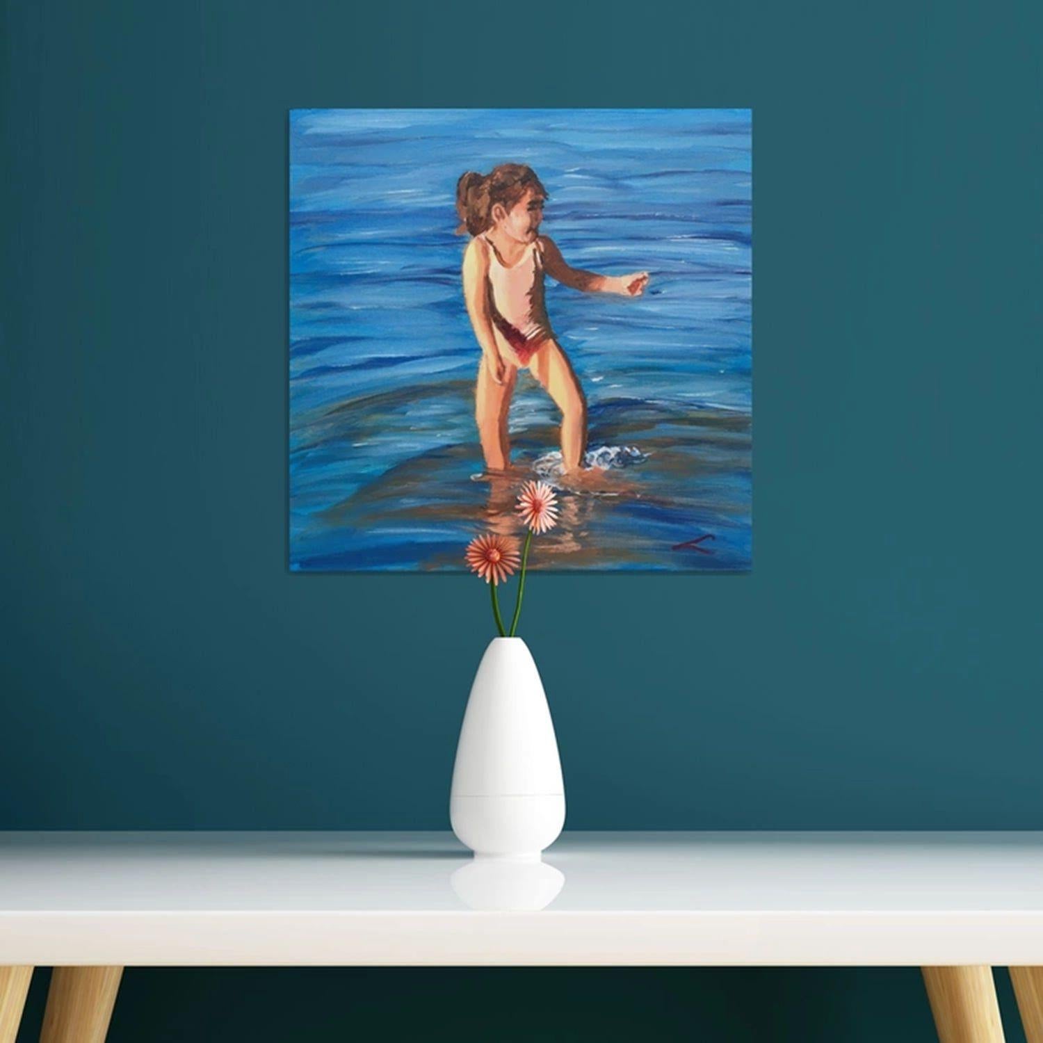 Ein junges Mädchen im Badeanzug steht knietief im Meer und hat die Haare zu einem Pferdeschwanz zurückgebunden. Sie zeigt nach vorne, wodurch sich das Wasser um ihre Beine herum kräuselt. Das Bild fängt einen spielerischen und fröhlichen Moment ein,