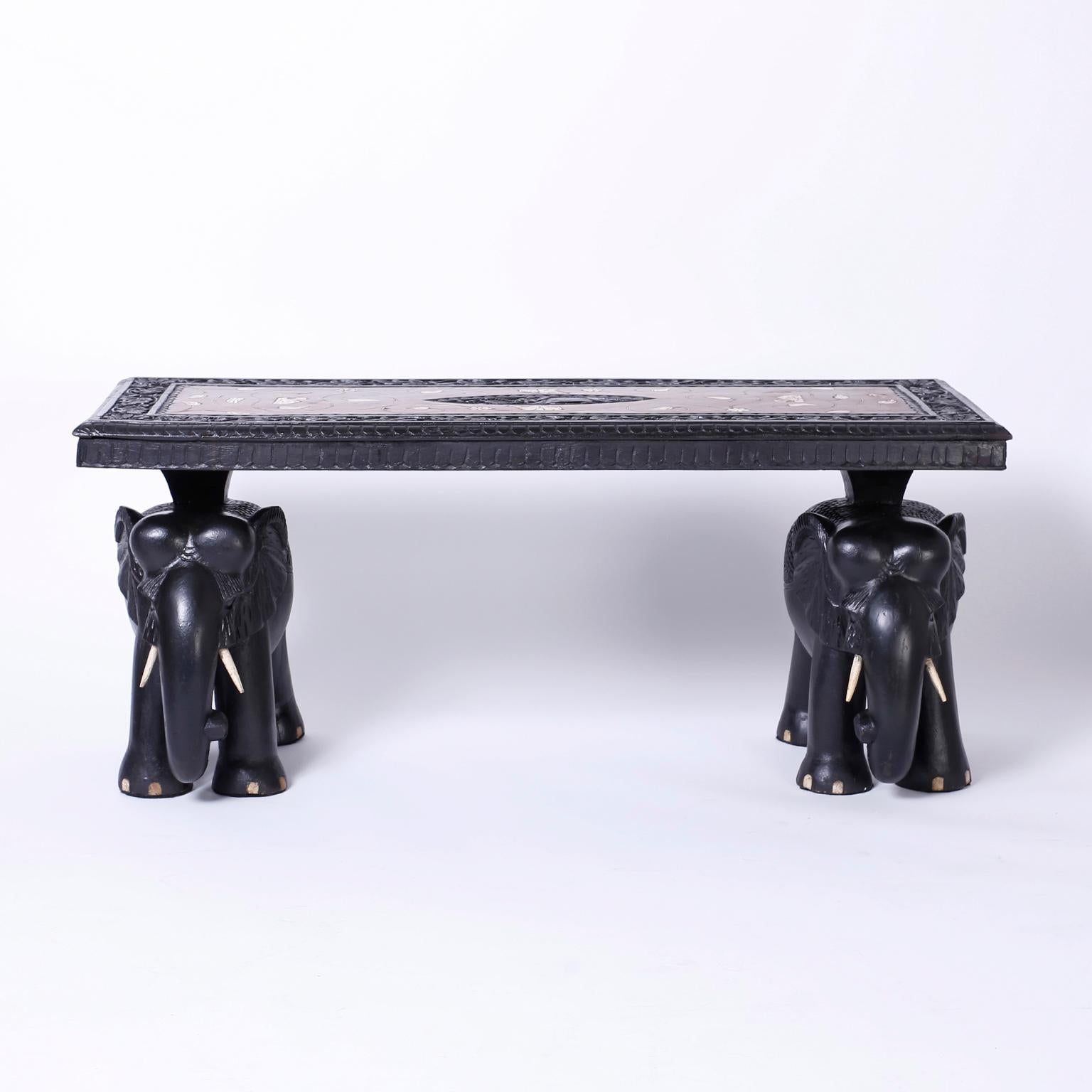 Antique Anglo Indian ebonized mahogany coffee table featuring an intricately carved top with bone inlays in an exposed grain panel, and a pair of carved and ebonized elephants as a base.