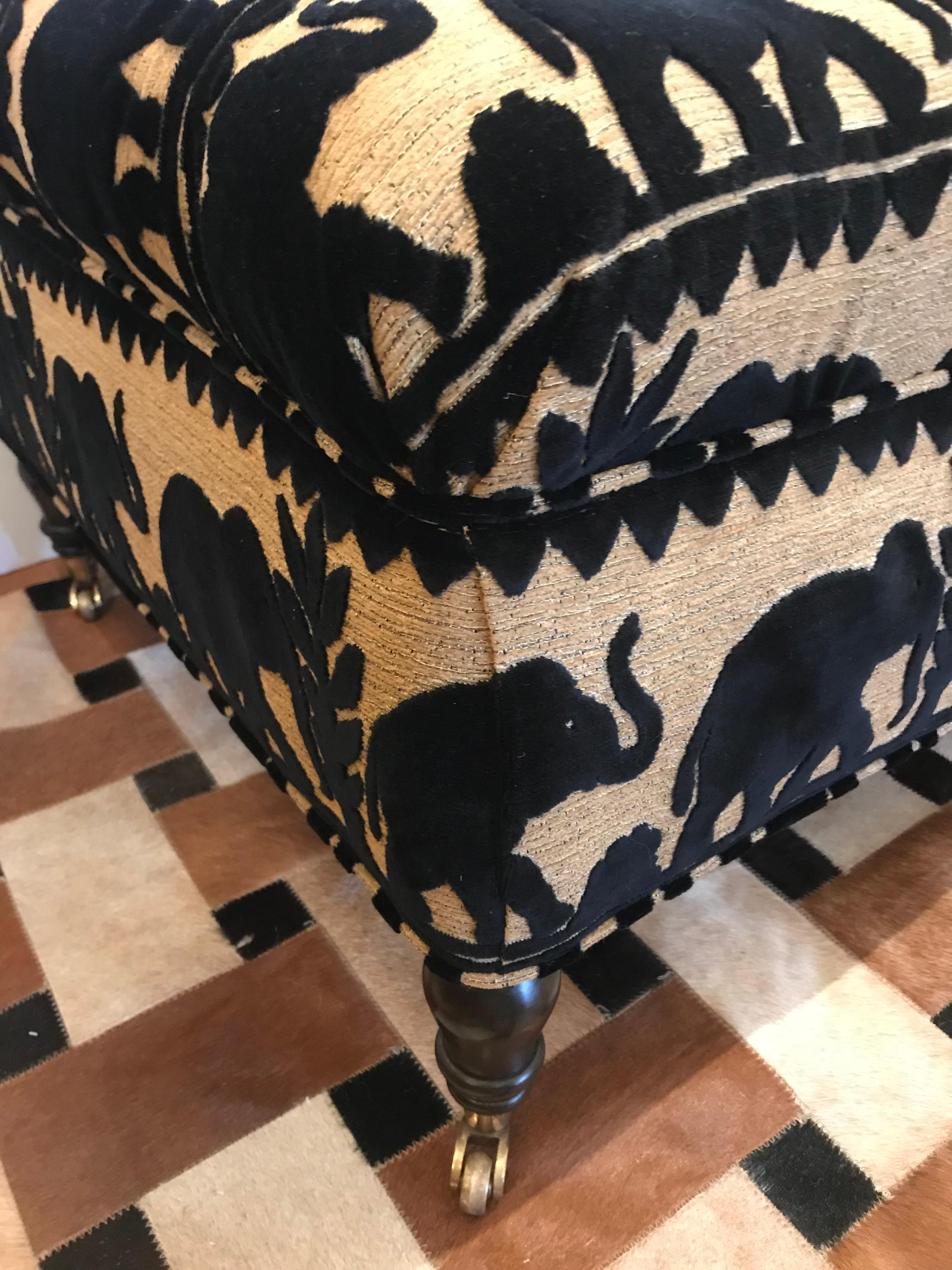 Striking Chesterfield style ottoman newly upholstered in a brown and black cotton fabric with an elephant motif. Ottoman has turned mahogany legs and casters.