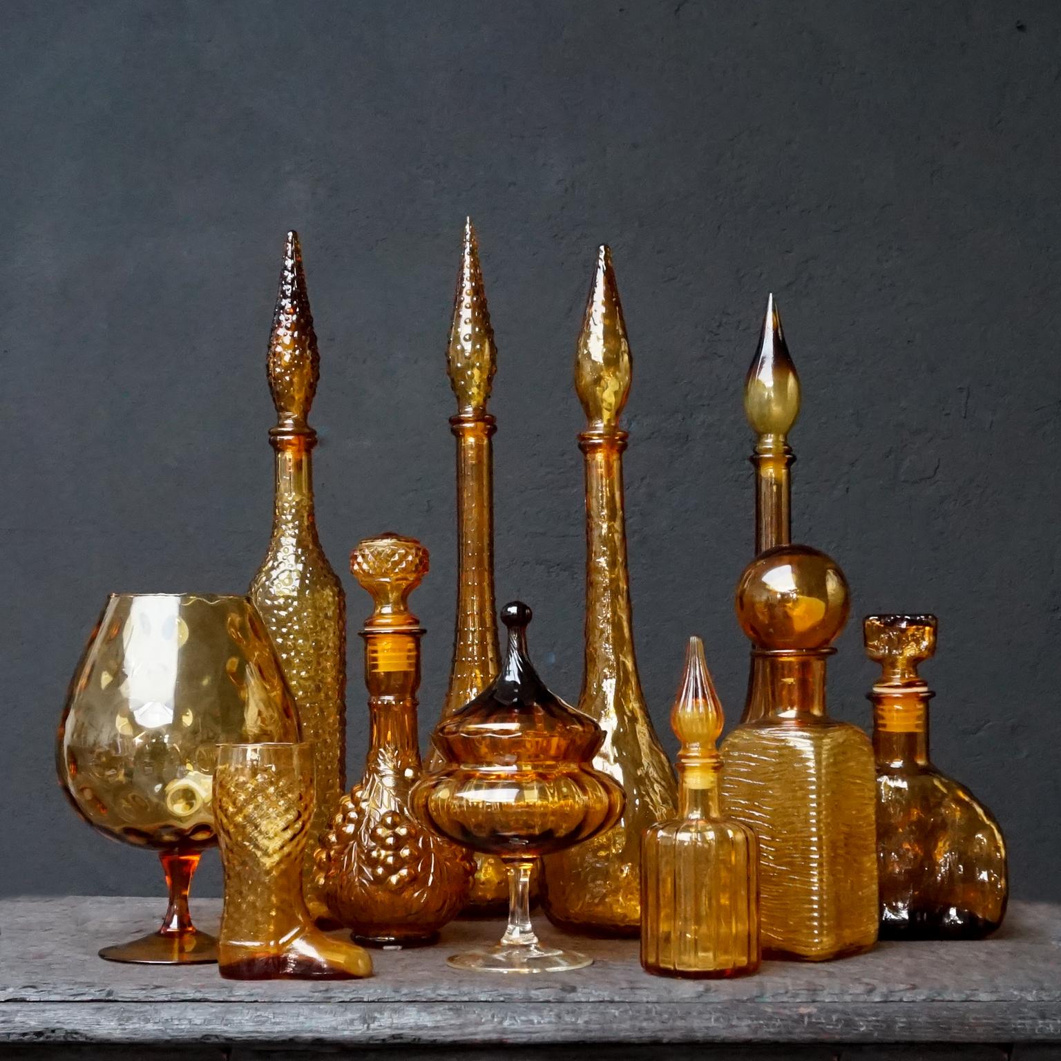 Very decorative amber or caramel brown yellow set of eleven different size and colour Italian glass Rossini Empoli bottles.
Nine pressed bottles, of which five genie bottles. Two blown clear glass items; a large cognac glass and a tent shape lidded