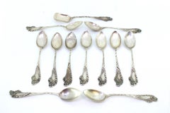 Eleven silver teaspoons and sugar scoop with reliefs and monogram handles