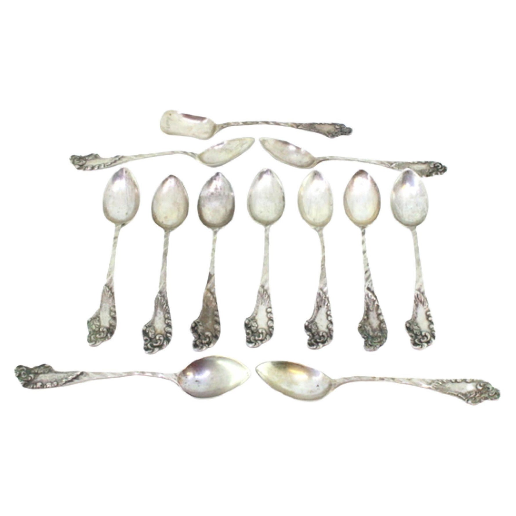 Eleven silver teaspoons and sugar scoop with reliefs and monogram handles