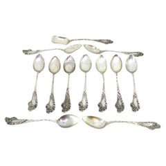 Eleven silver teaspoons and sugar scoop with reliefs and monogram handles