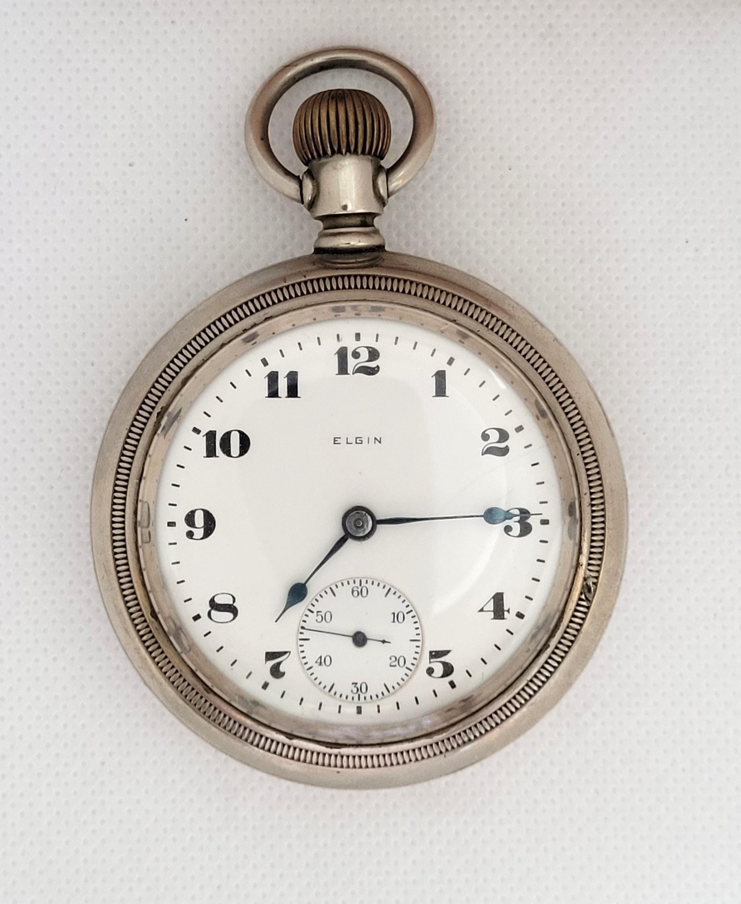 Elgin 1921 railroad pocket watch with a 59mm case made of silverode and is 20mm thick. Heavy watch with a clean plastic crystal. The case has a minor blemish and a light hand carving that could be polished. The movement is 7 jewel, working, and