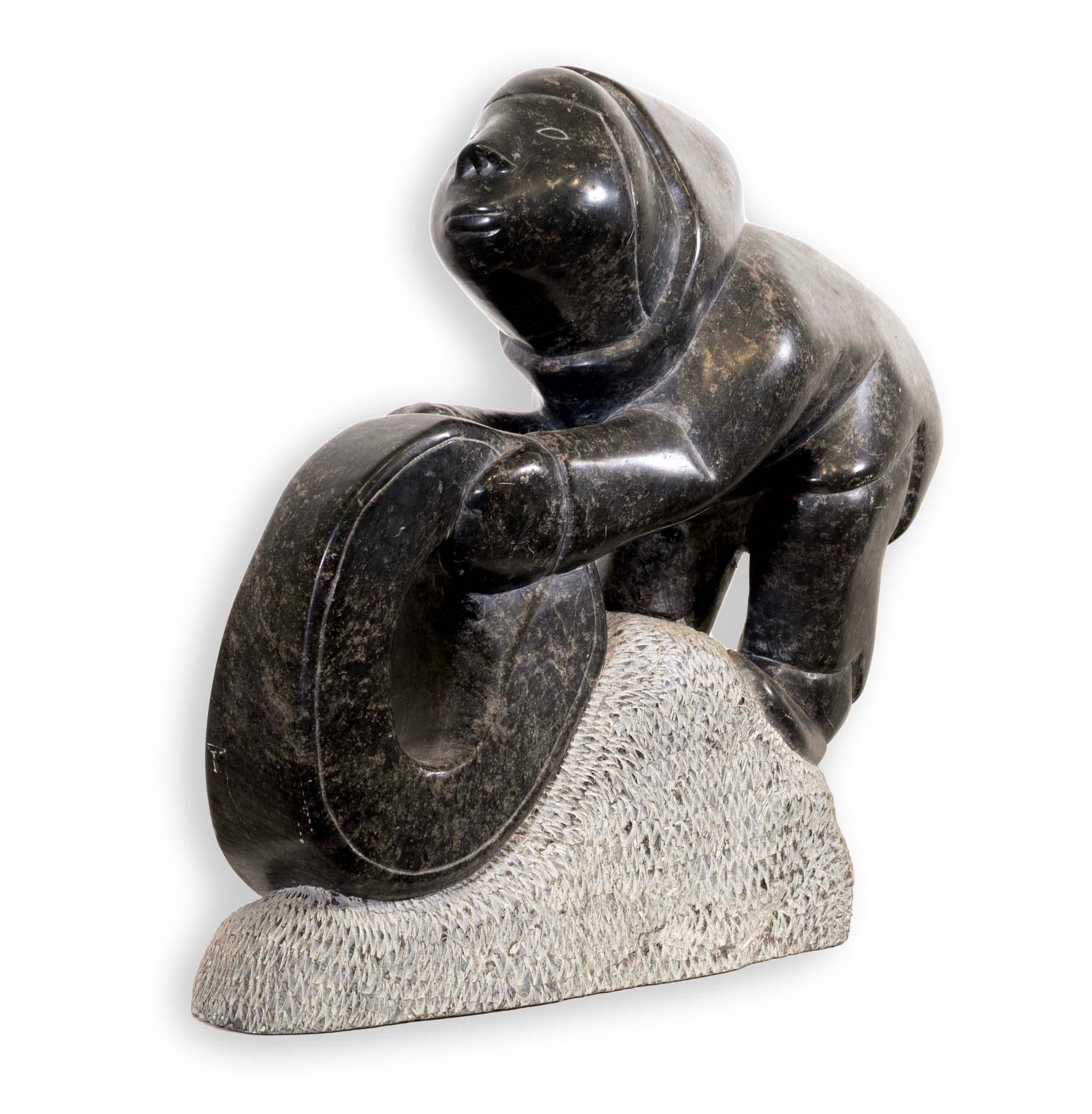 An Inuit figurative soapstone carving sculpture by the Povungnituk Cooperative. From the Quebec region in the Canadian Artic. Circa 1980s. The figure is holding a circular item which creates a sense of movement and energy. Elijassiapikwas born near