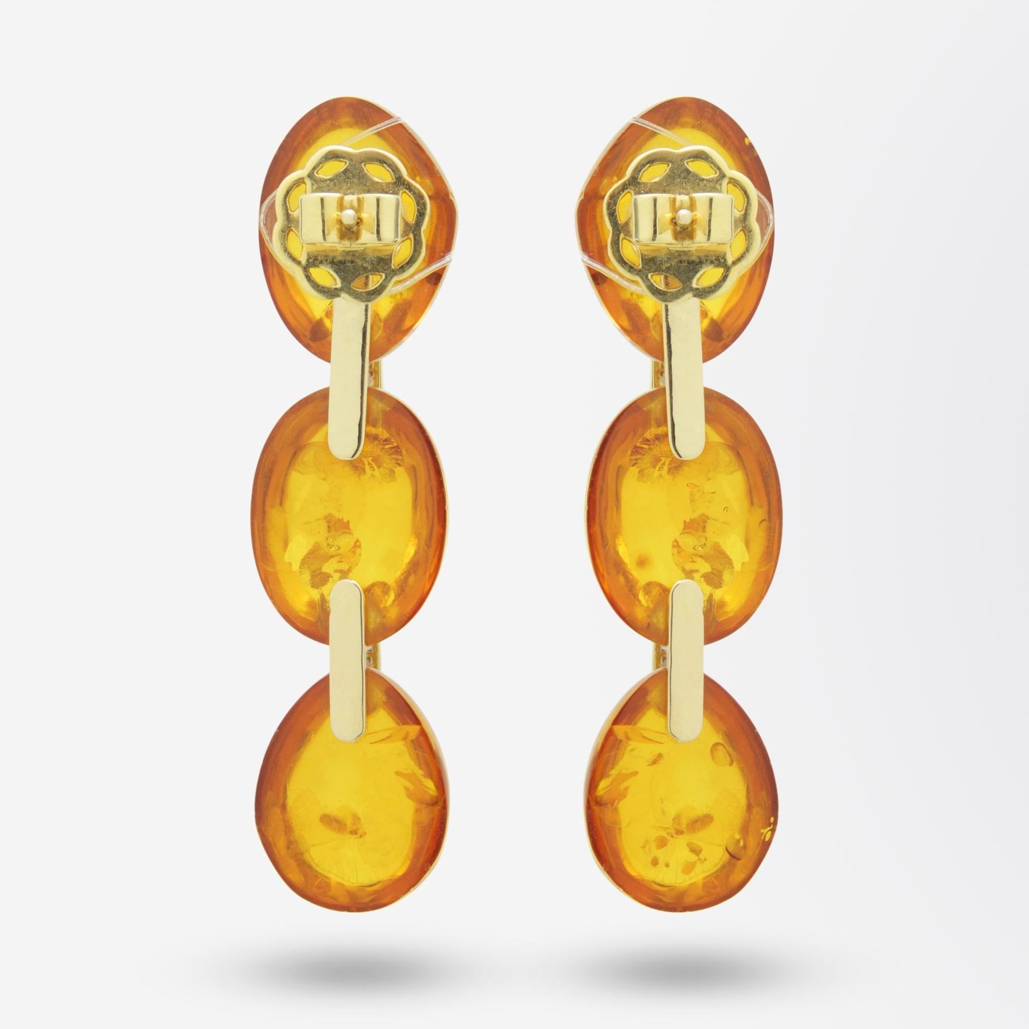 A pair of drop earrings crafted from 18 karat gold, diamonds and amber. The stud drop earrings are formed with three highly polished pieces of cabochon amber which are connected by links of 18 karat yellow gold set with brilliant cut diamonds. The
