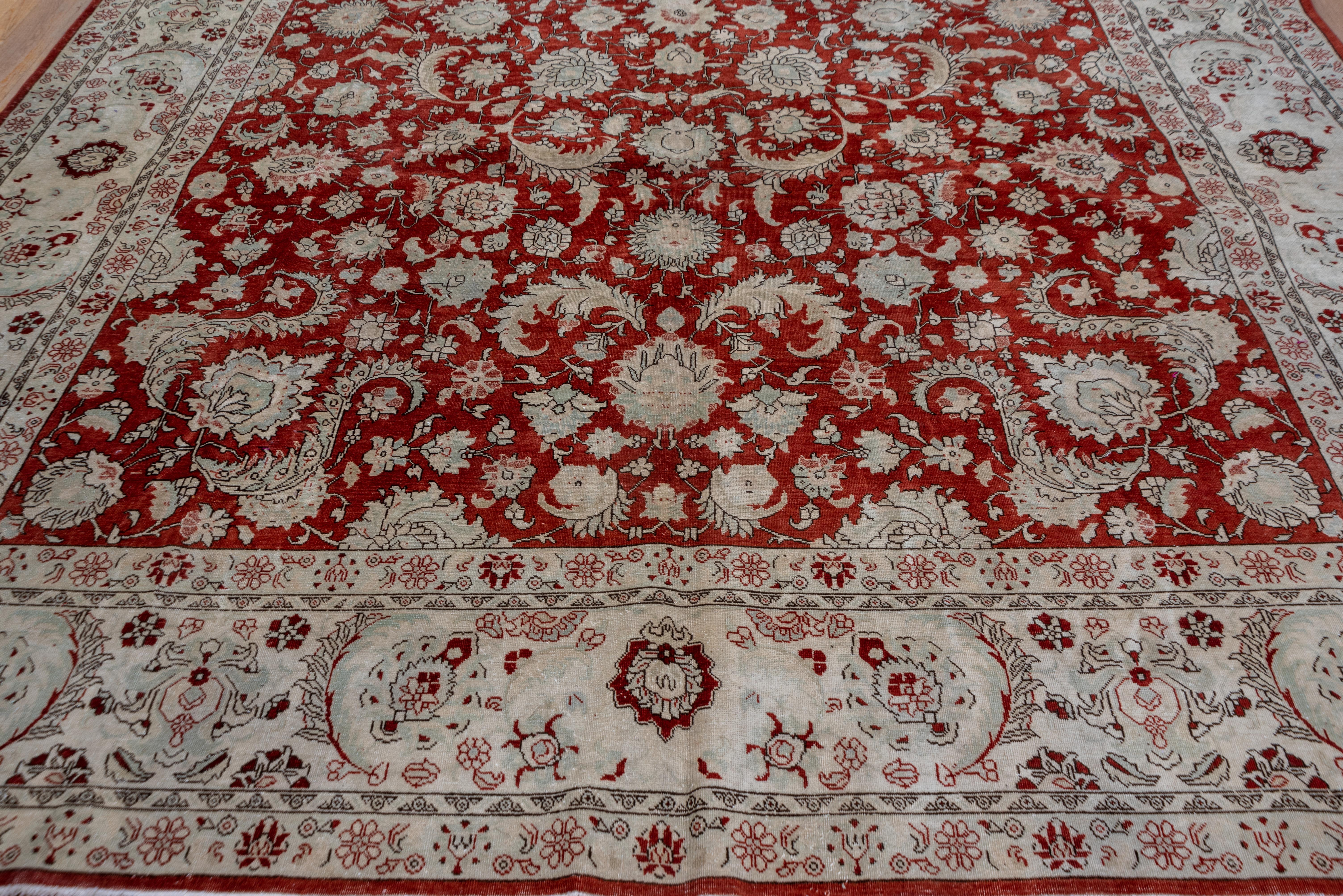 This well-woven Persian Tabriz carpet shows a rich red field fully covered by an allover design of curling and barbed leaves, petal palmettes, rosettes and smaller vegetal devices. The mushroom border presents dark palmettes and barbed sickle leaves