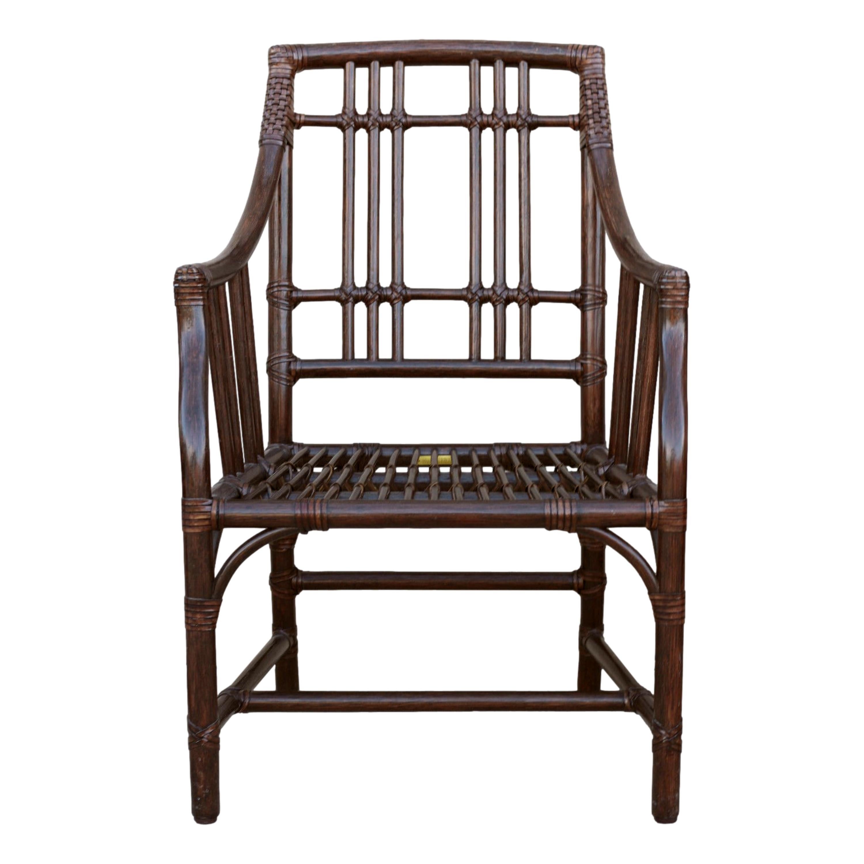 A pair of McGuire Balboa Rattan Arm Chairs or Dining Chairs. Featuring Craftsman details, the Balboa Arm Chair, designed by Elinor McGuire, is a classic form that could fit many different spaces. Chairs have a rich dark tobacco finish, and the