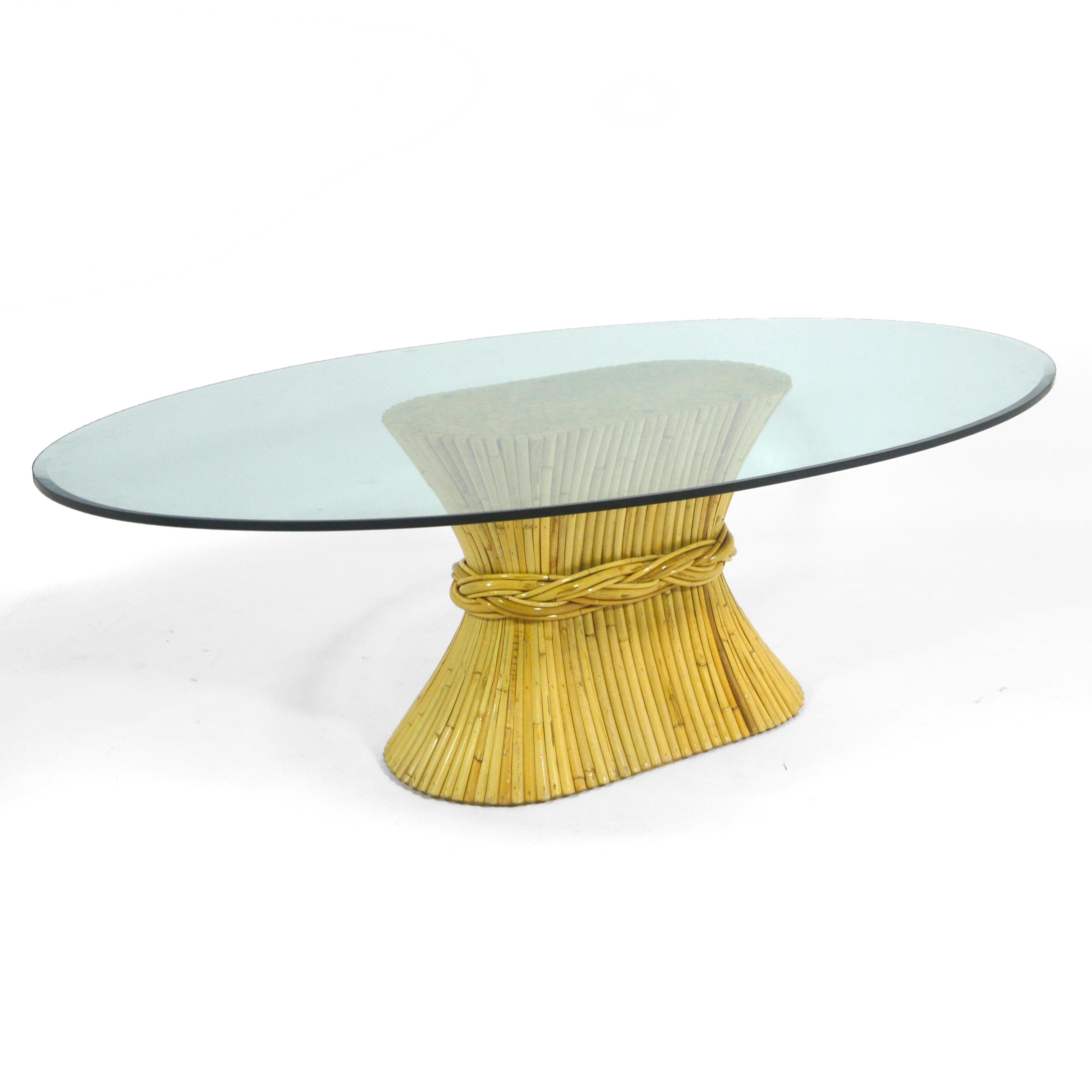 One of Elinor McGuire's most iconic and enduring designs for McGuire of San Fransisco, the NP-12 dining table has a base of rattan gathered at the waist like a sheaf of wheat that supports an elegant elliptical glass top with a beveled edge detail.