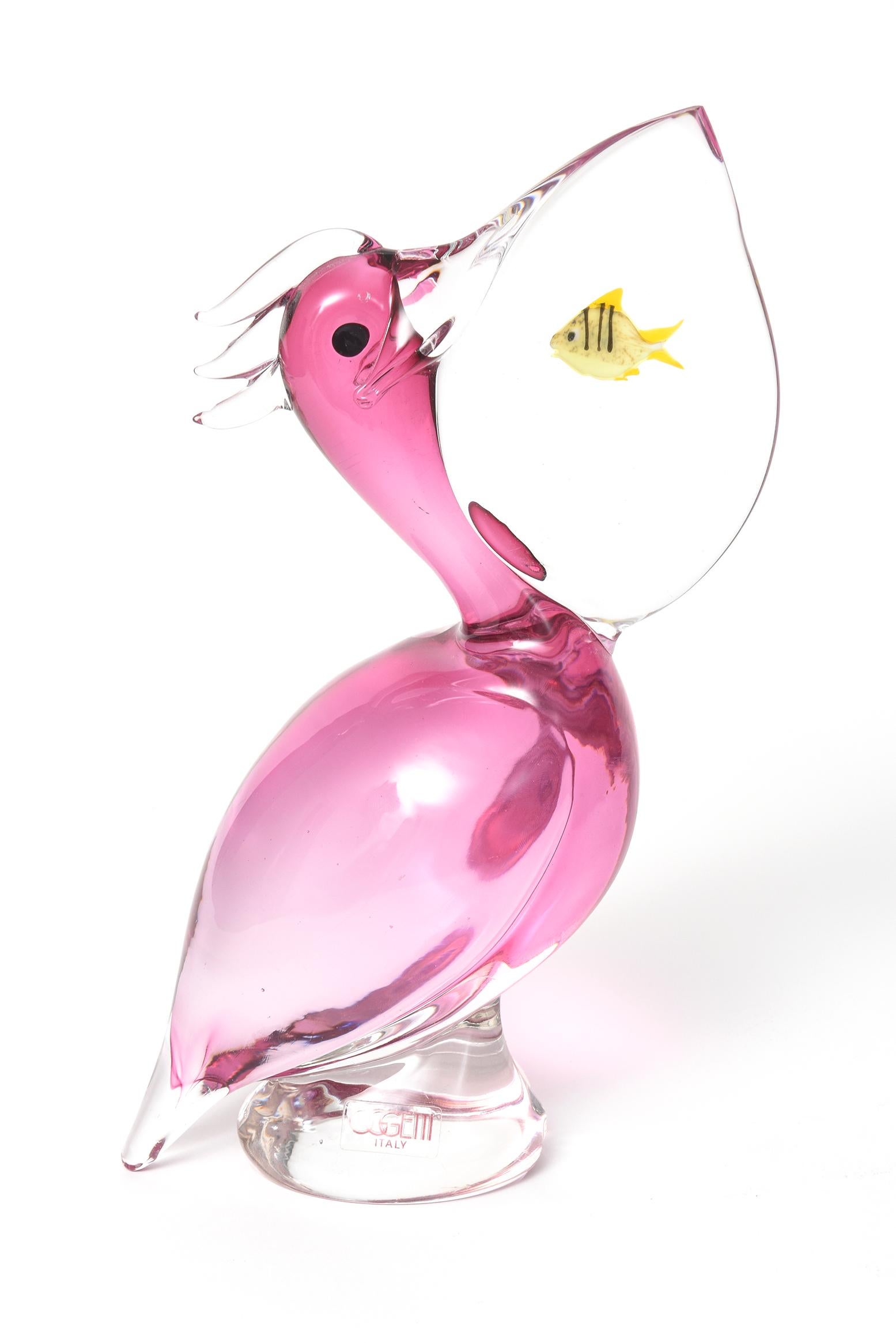Oggetti Italian Murano glass pelican features a pink hued body and transparent bill with a small yellow fish inside of it. Marked with a sticker Oggetti Italy. Signed on bottom by Elio Raffaeli

Oggetti was founded in 1975 and initially their