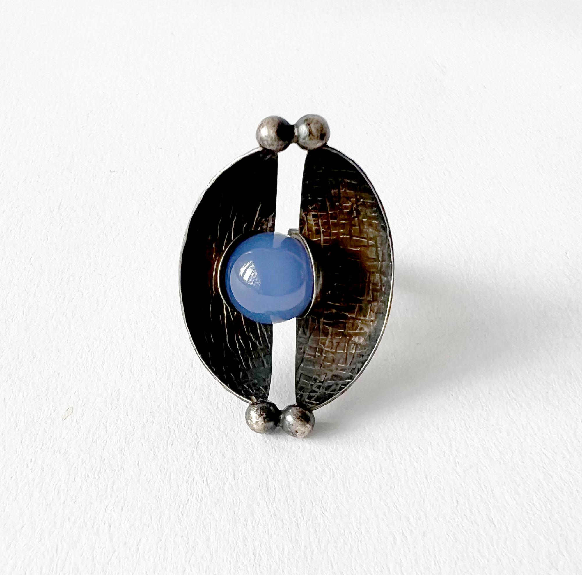 Ring aus geschwärztem Sterlingsilber und natürlichen Edelsteinen, entworfen von Elis Kauppi für Kupitaan Kulta in Turku, Finnland. Der Ring besteht aus zwei schalenförmigen Segmenten mit geätzter Textur auf beiden Seiten, die eine Chalzedonkugel