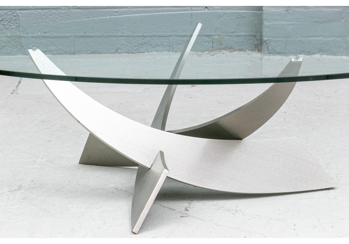 Constructed from thick solid steel with a lustrous champagne-plated finish, this elegant design mimics a piece between sculpture rather than furniture. The table features three interlocking arms, reaching up to support the thick glass top, which are