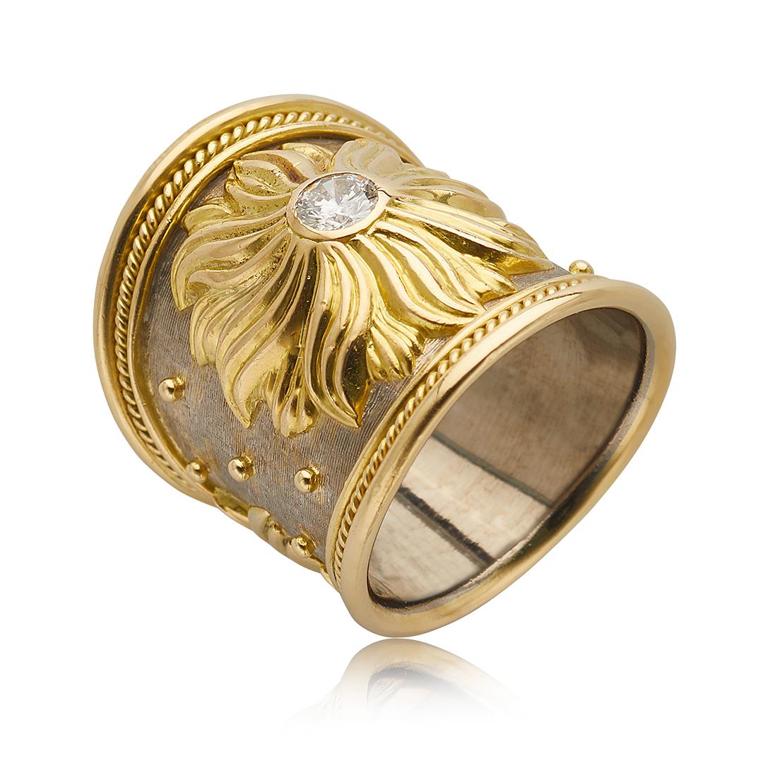 This wide band ring by Elizabeth Gage is crafted from both 18 karat yellow and white gold, and features a sun motif with a round cut diamond weighing 0.30 carats at its center. The diamonds has G coloring and SI2 clarity. The band is tapered,