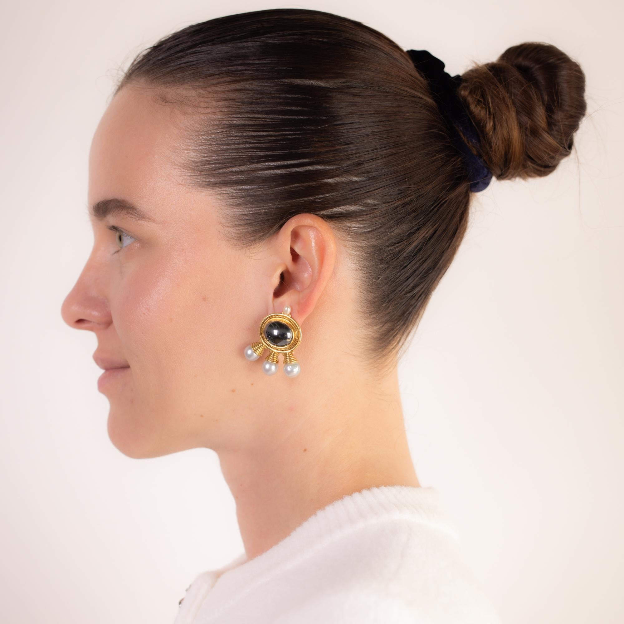 These vintage Elizabeth Gage earrings exude bold elegance, featuring two 16mm cabochon-cut hematites complemented by eight cultured pearls ranging from 8.95mm to 5mm. Crafted in rich 18k yellow gold, they showcase the designer’s signature artistry
