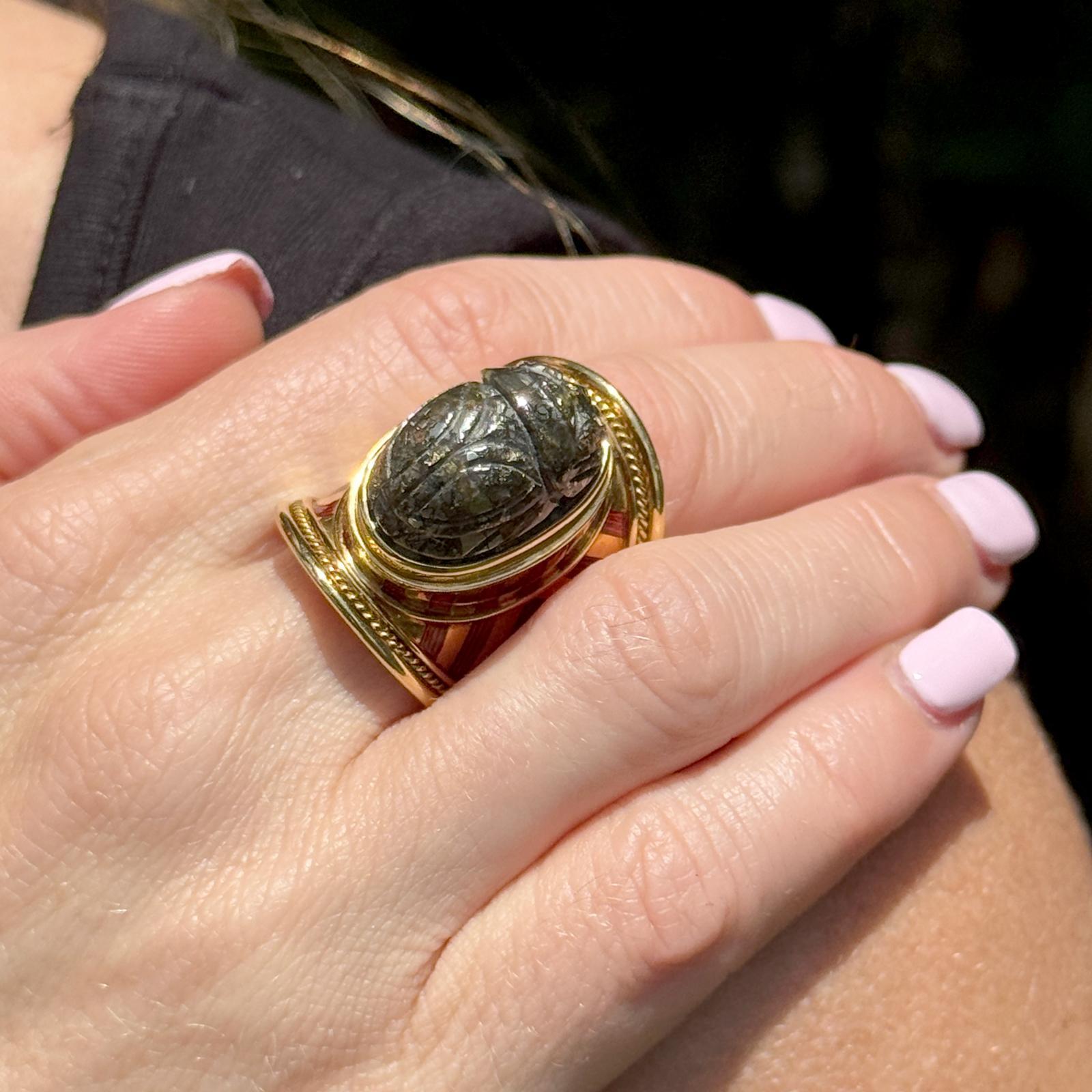 This extraordinary statement ring by Elizabeth Gage features a beautifully carved labradorite scarab set in rich 18 karat yellow gold, accented with striking red enamel detailing. A true work of art, the ring showcases the designer's signature