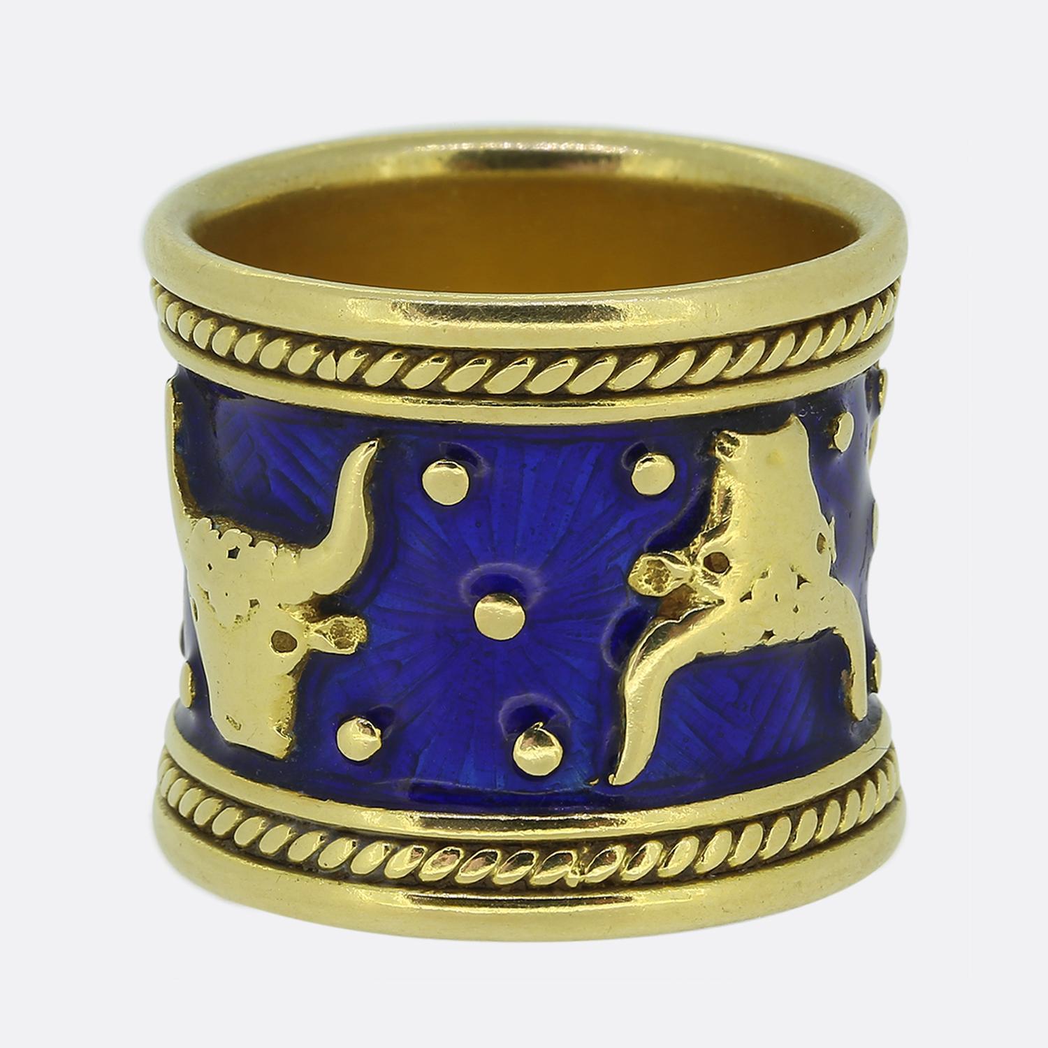 Here we have a distinctive piece from renowned British jewellery designer, Elizabeth Gage. Crafted from 18ct yellow gold, this wide band features a bold design with deep blue enamel, adorned with gold bull motifs and circular accents. The intricate