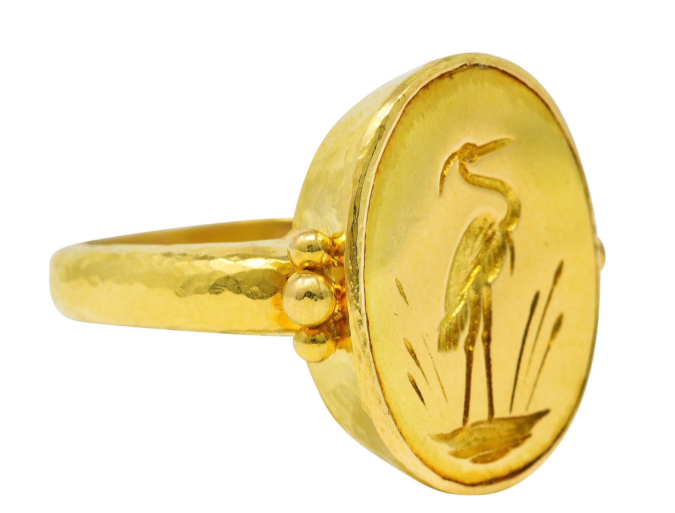 Ring centers an engraved gold oval intaglio depicting a crane wading through fronds. Flanked by beaded gold shoulders. With hammered gold texture throughout. Stamped 19k for 19 karat gold. With maker's mark for Elizabeth Locke. Circa: 21st century.