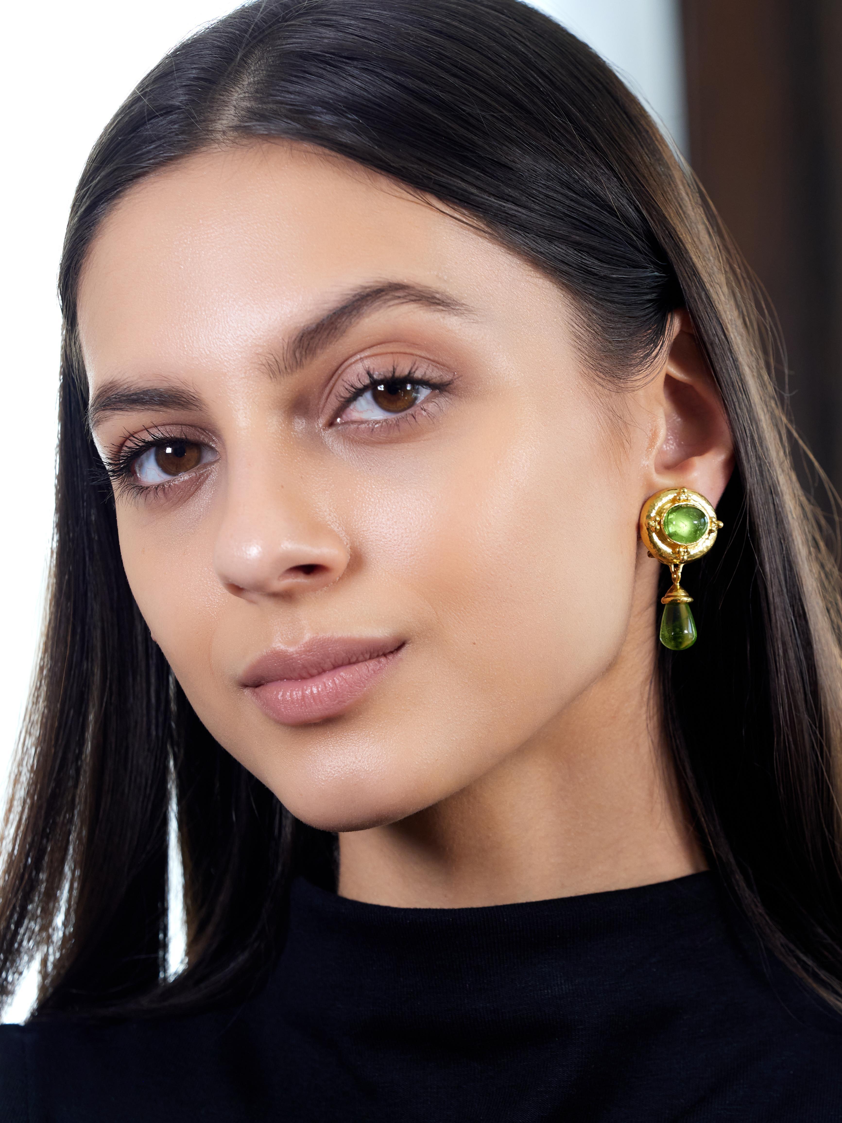 Designed as oval shaped surmounts suspending removable articulating drops
Centering an oval shaped peridot cabochon measuring 9.5 x 11.5 mm
Transparent bright medium yellow green and bezel set
Backed by mother-of-pearl - white and iridescent
With a