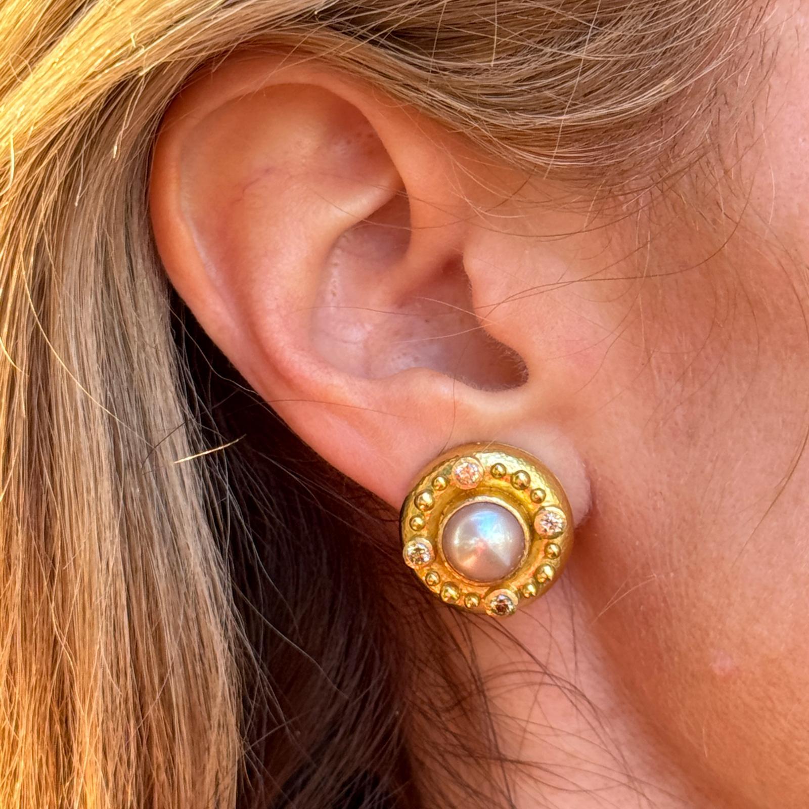 The Elizabeth Locke 19 karat yellow gold pearl and diamond earrings feature elegant 20mm round settings, each showcasing a luminous pearl center encircled by 8 sparkling round brilliant-cut diamonds. These earrings are signed 