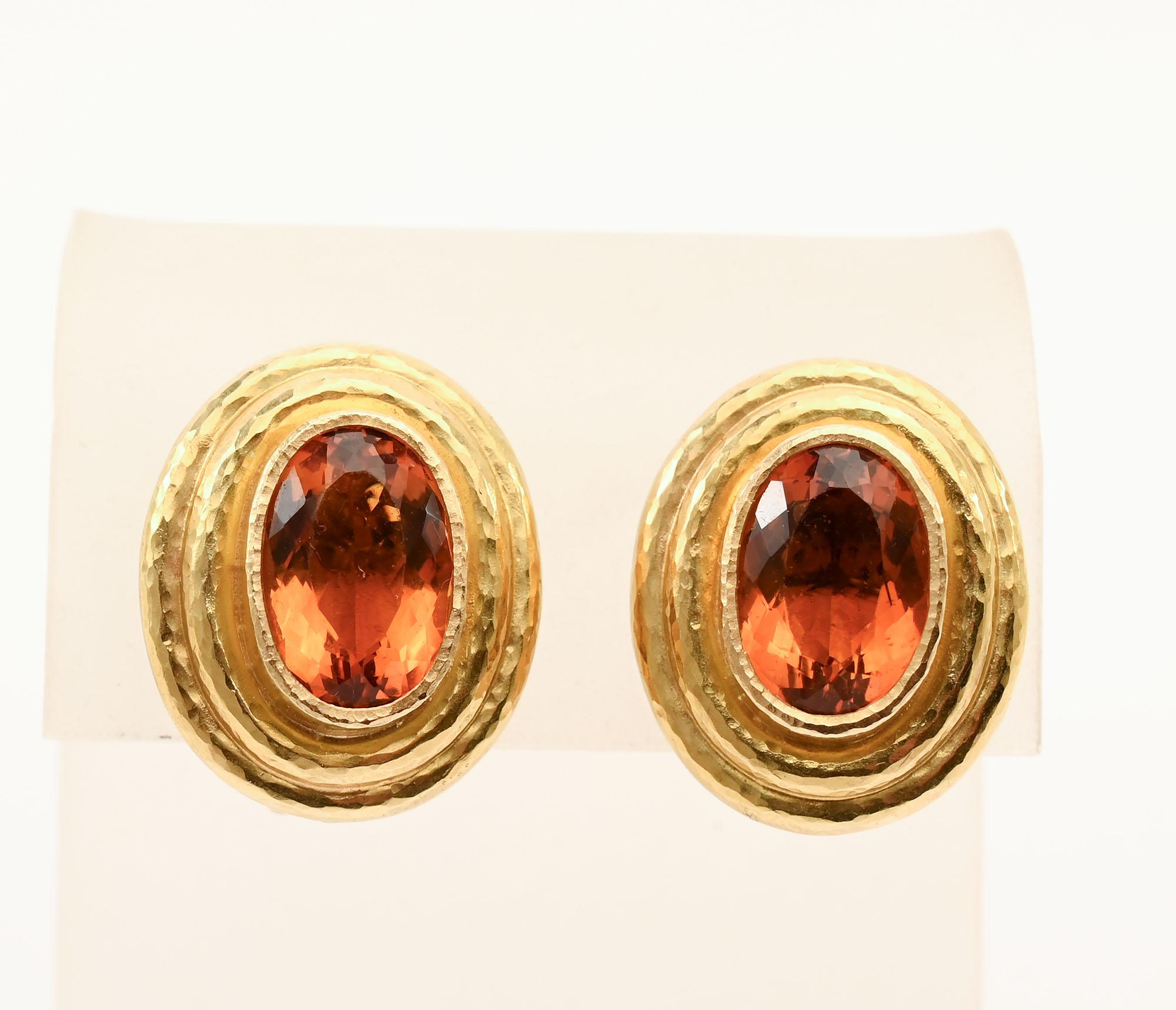 Orecchini d'oro di Elizabeth Locke con un ovale  pietra citrina sfaccettata incastonata in ognuno di essi. Le pietre color miele sono incastonate in un castone con due fasce a gradini. Le fasce hanno la finitura in oro martellato che Locke utilizza