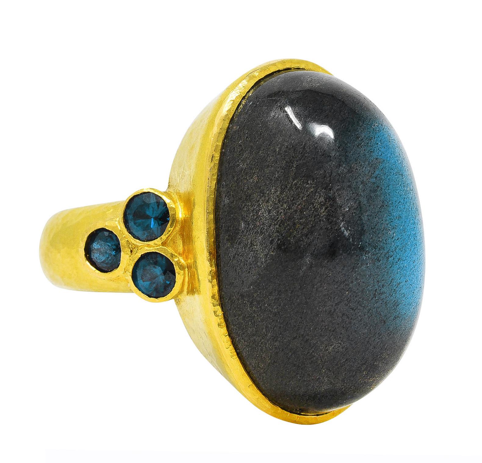Featuring a substantial oval cabochon of labradorite measuring approximately 23.0 x 14.5 mm

Translucent gray in body color with very strong labradorescence exhibited as a broad blue flash with scintillation

Bezel set in a hammered gold surround