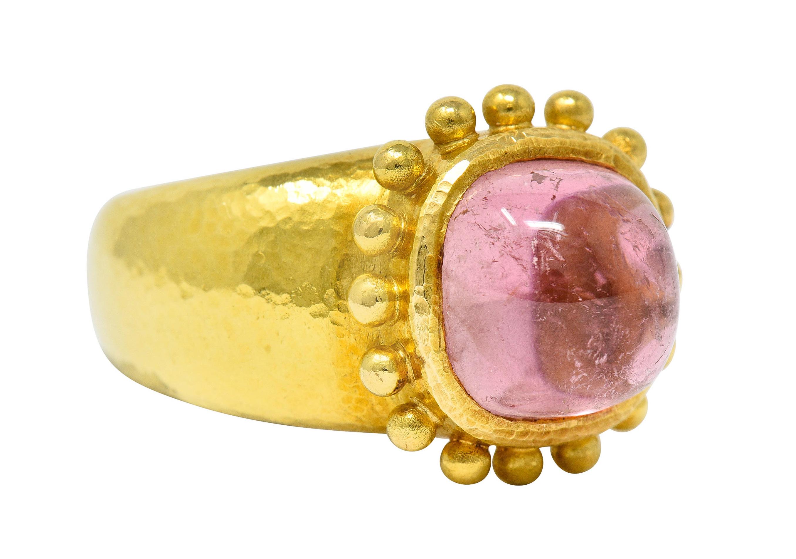 Centering a sugarloaf cabochon of pink tourmaline that measures 10.0 x 10.0

Semi-transparent and medium light pink with natural inclusions and moderate chatoyancy

Bezel set and with a prominent gold bead halo and a subtle hammered finish

Stamped