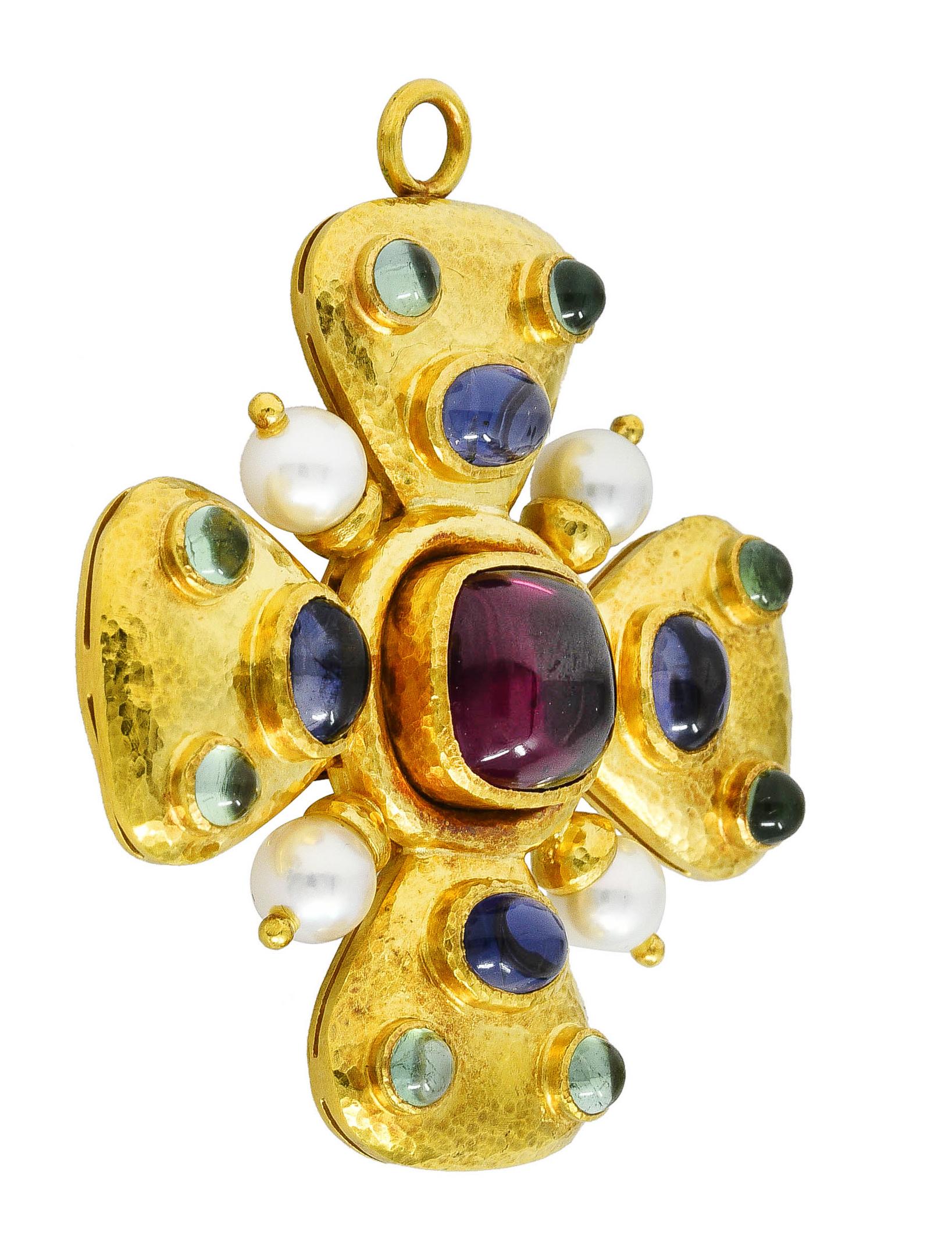 Pendant brooch is designed as a puffed form maltese cross with a strongly hammered finish. Centering a sugarloaf cabochon rhodolite garnet measuring approximately 10.5 x 10.5 mm - eye clean and purplish red in color. With oval iolite cabochons