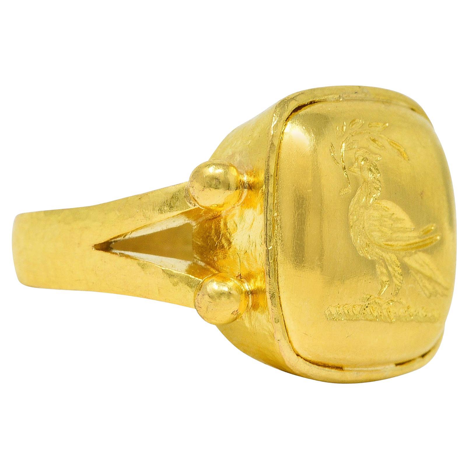 Ring centers a high polished gold cushion shaped intaglio

Depicting a pheasant holding an olive branch in its beak

Flanked by split shoulders with gold beading

With hammered gold texture throughout

Stamped 19k for 19 karat gold

With maker's