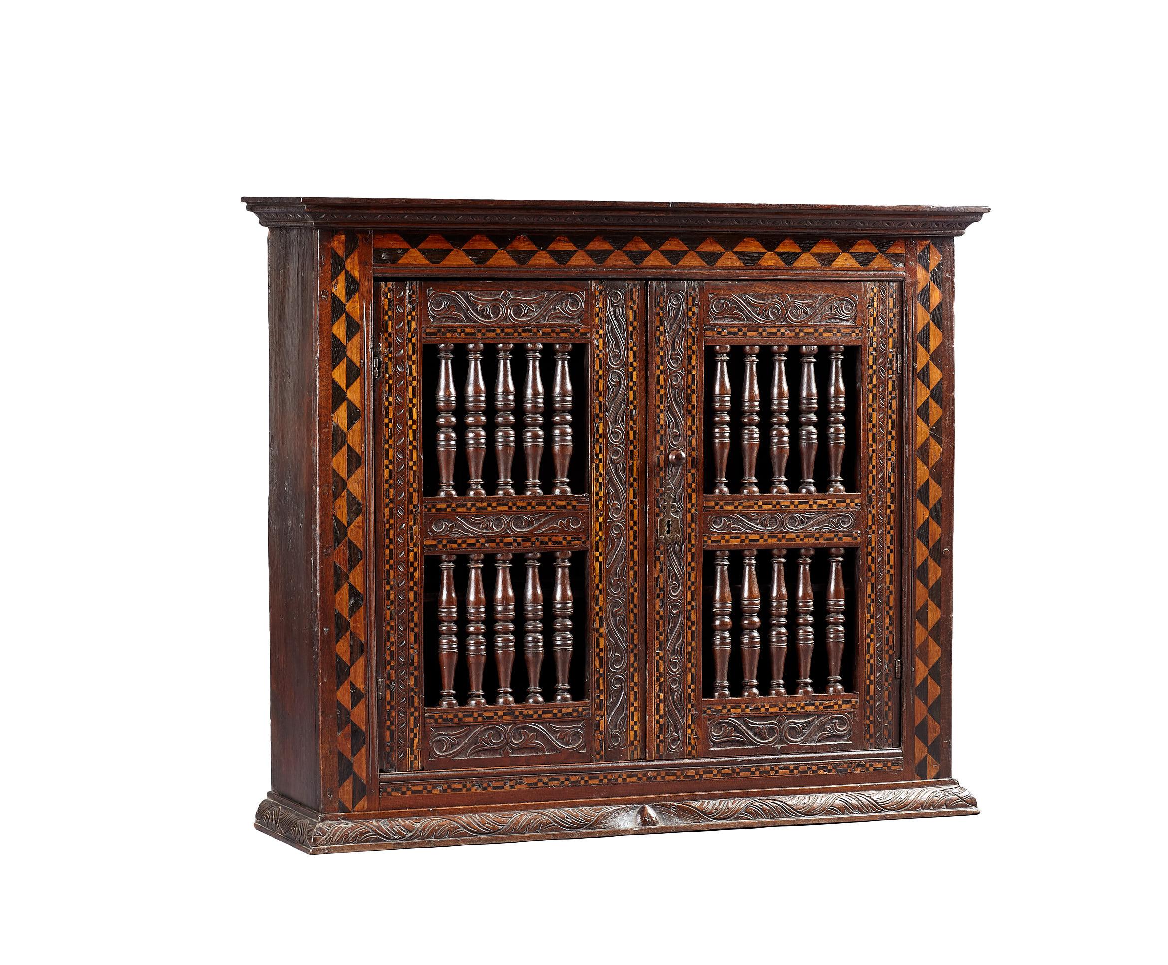 Late Elizabethan Inlaid Oak Mural wall or glass cupboard, English circa 1590 - 1600.

The joined framed wall cupboard with carved cornice above contrasting chevron inlays of Bog Oak & Holly, with twin spindle filled doors, further floral interlace