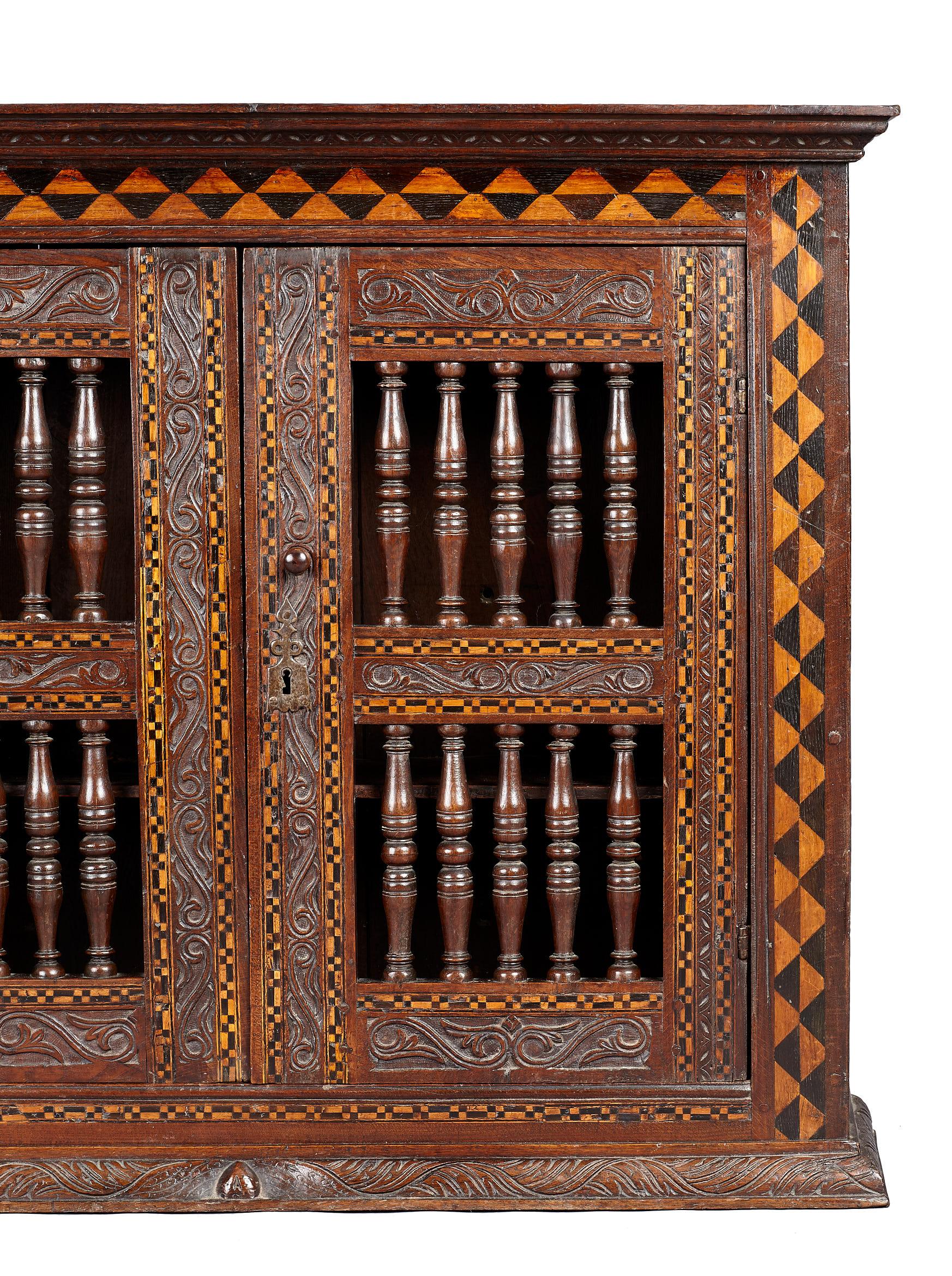 Late Elizabethan inlaid oak mural wall or glass cupboard, English, circa 1590-1600.

The joined framed wall cupboard with carved cornice above contrasting chevron inlays of bog oak and holly, with twin spindle filled doors, further floral