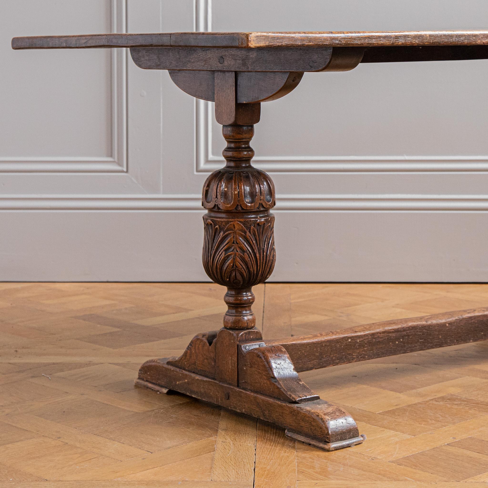 Table à tréteaux en chêne de style élisabéthain, début du 20e siècle ; le plateau rectangulaire repose sur des supports jumeaux en forme de nopes, de lobes, de feuillages sculptés et d'encorbellements ; les tréteaux sont reliés par une entretoise.