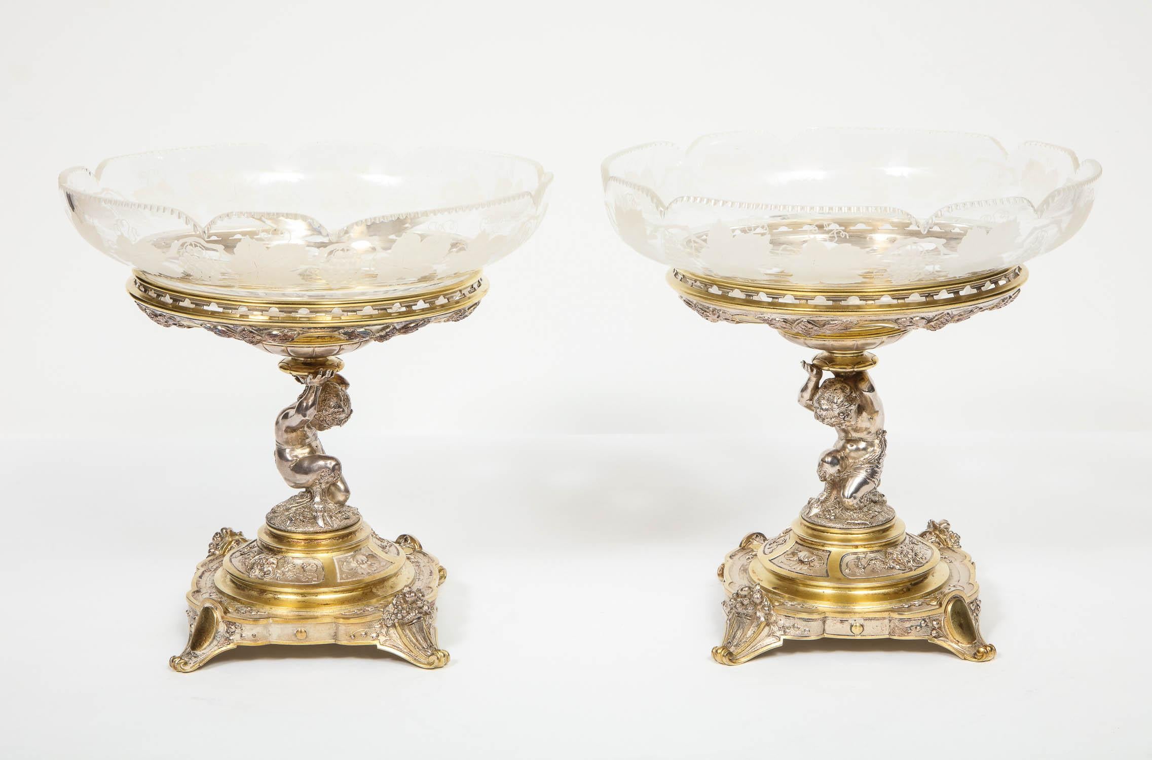 Elkington & Co., a pair of gilt and silvered bronze tazza centerpieces with original etched glass bowls.

Victorian period, Birmingham, England, circa 1867-1868.

The bowls finely etched with grapevine motif supported by figural stands in the